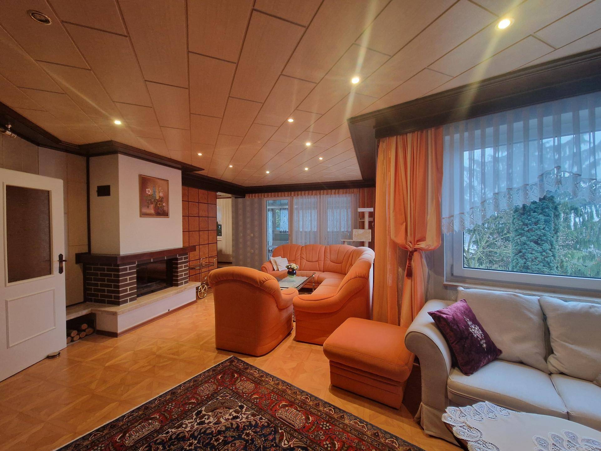 Gemütliches Wohnzimmer mit Kamin, orangefarbenen Sofas und Holzdeckenverkleidung.