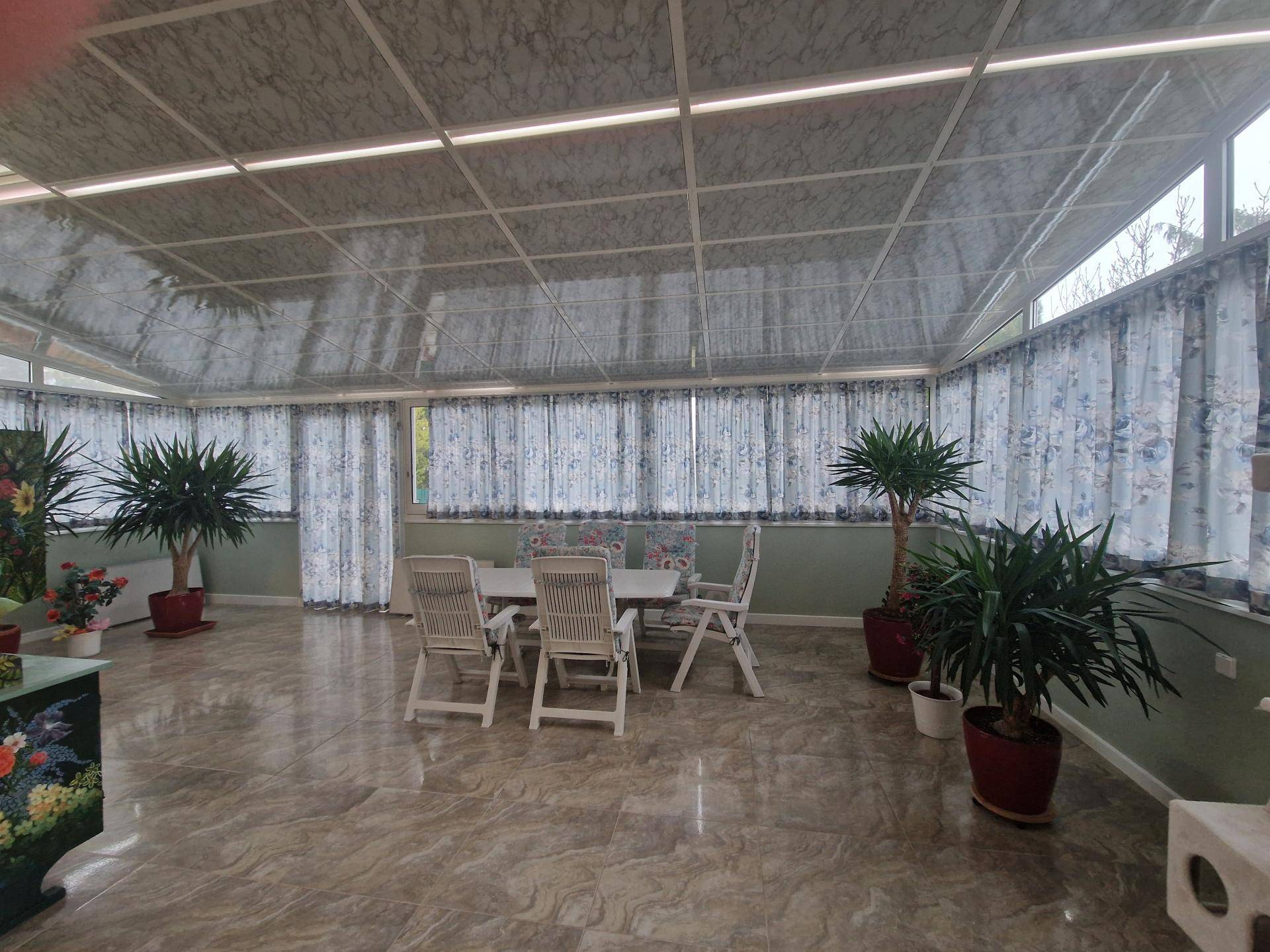 Heller Wintergarten mit Fliesenboden, Esstisch und vielen Pflanzen, ideal zum Entspannen.