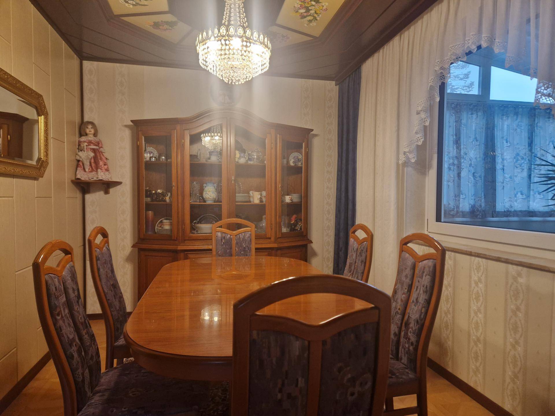 Klassisches Esszimmer mit großem Holztisch, passenden Stühlen und elegantem Kronleuchter.