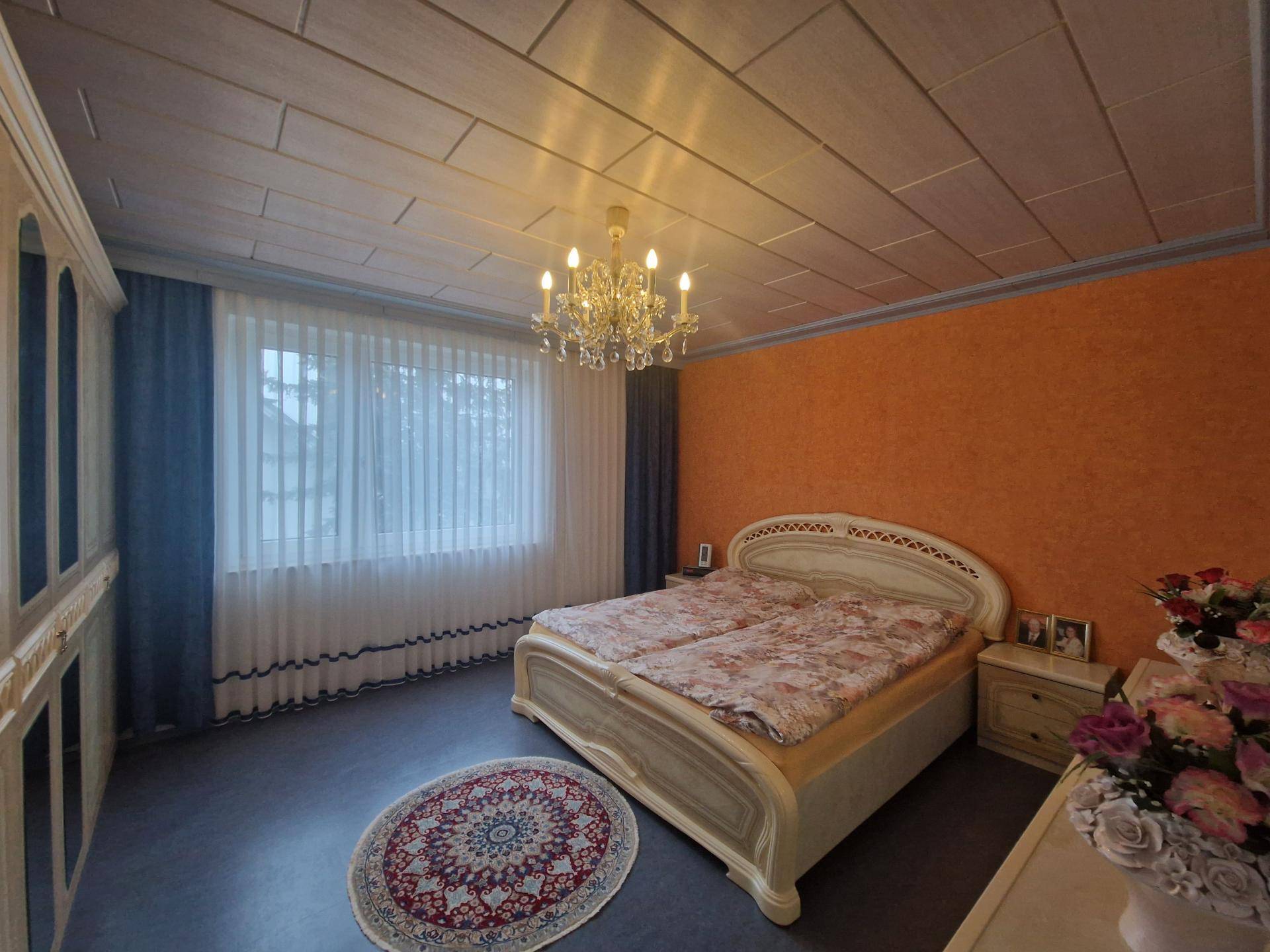 Schlafzimmer mit auffälliger orangefarbener Wand, Doppelbett und klassischem Kronleuchter.
