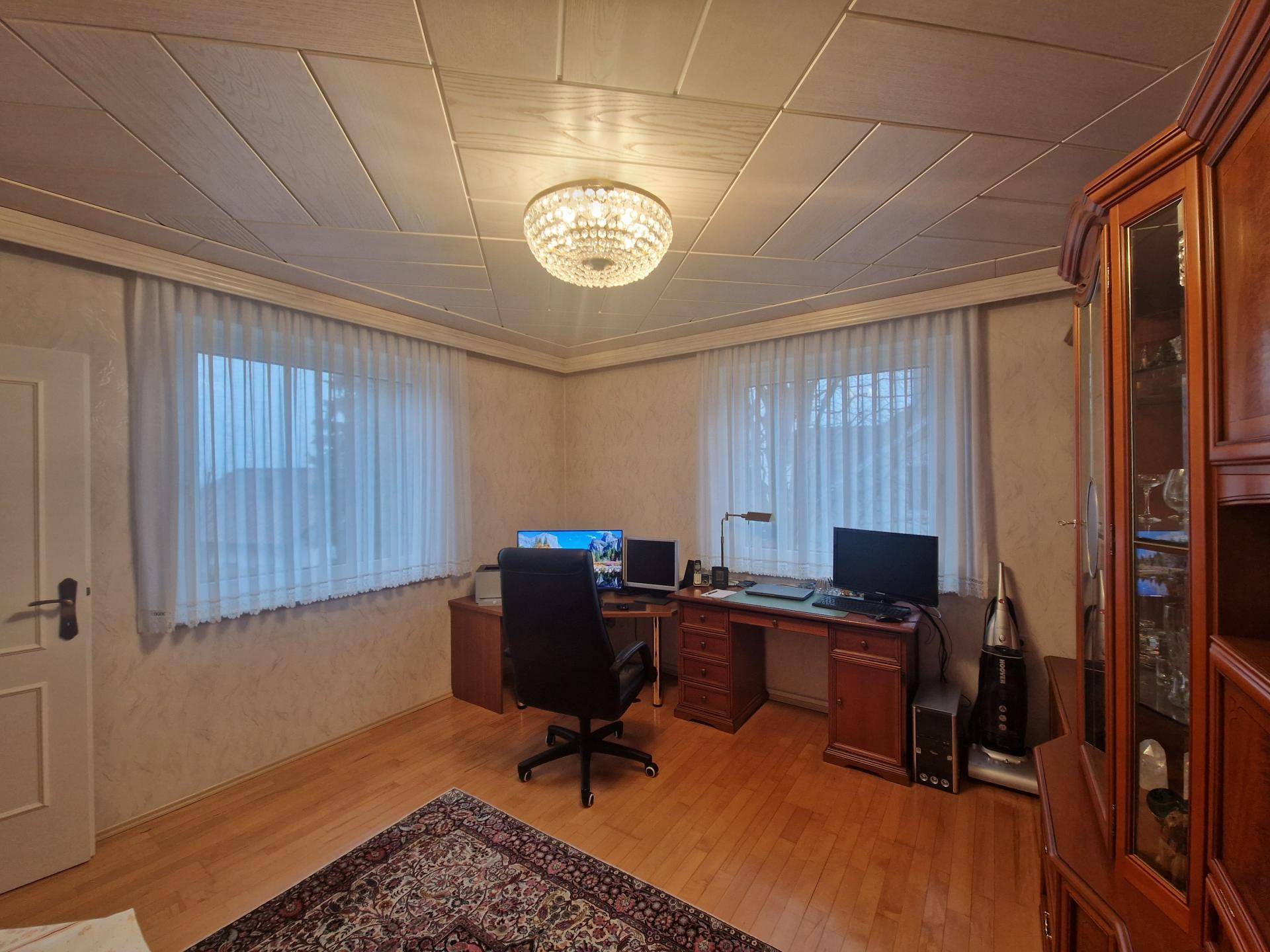Arbeitszimmer mit Holzschreibtisch, großem Schrank und Blick nach draußen.