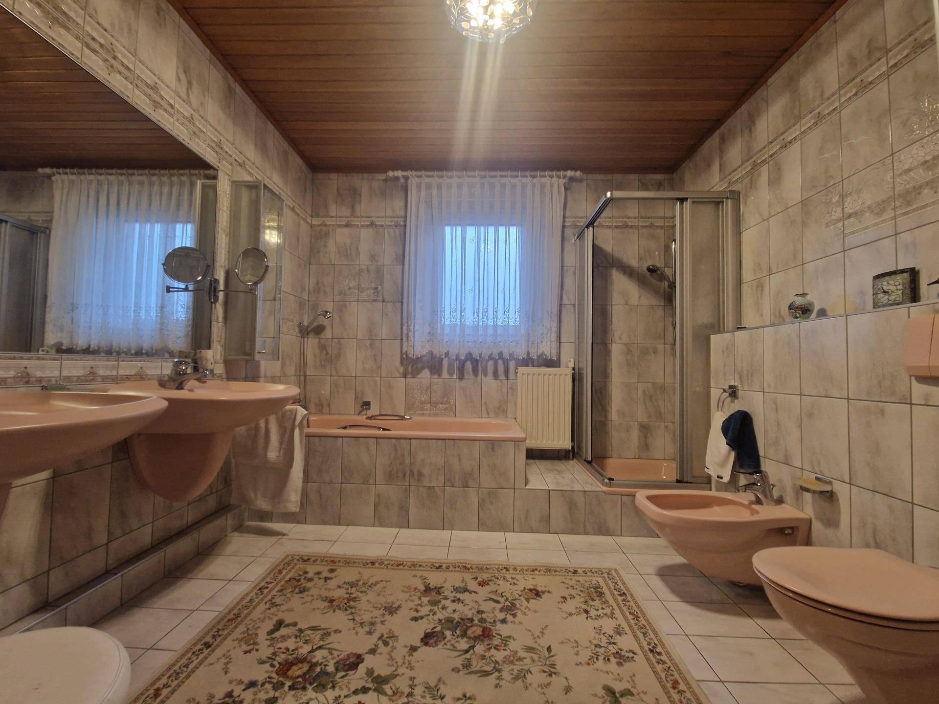 Badezimmer im 80er-Jahre-Stil mit rosa Sanitärobjekten, Fliesen und Duschkabine.