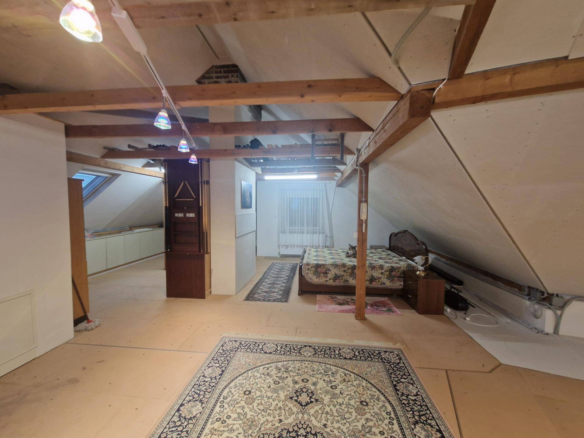 Großzügiger Dachbodenbereich mit Holzbalken, Schlafbereich und Teppichen.
