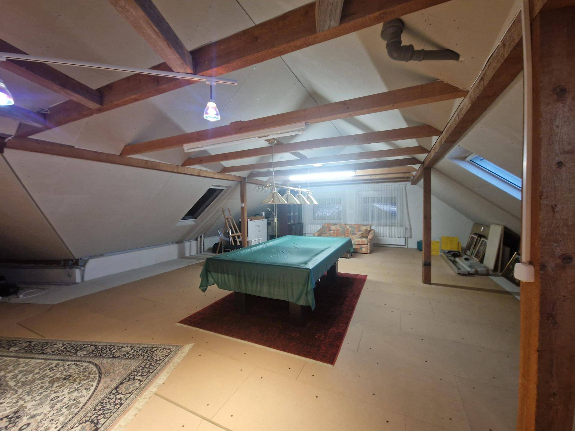 Ausgebauter Dachboden mit sichtbaren Holzbalken, Billardtisch und Dachfenstern.