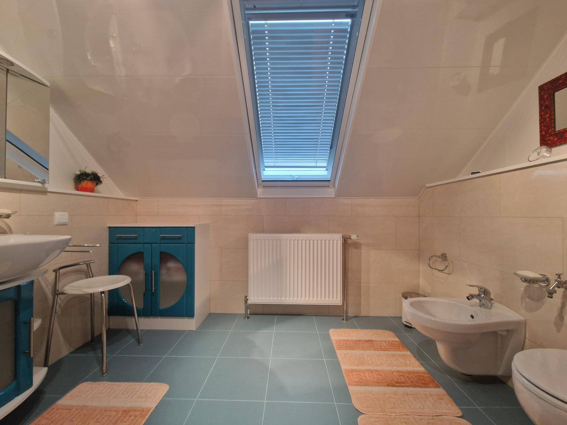 Helles Badezimmer im Dachgeschoss mit Dachfenster, Bidet und blauen Bodenfliesen.