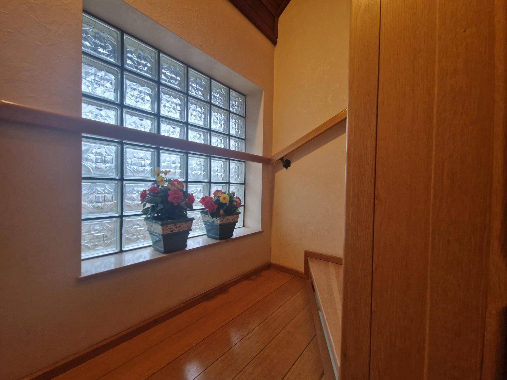 Treppenhaus mit Glasbausteinfenster, Holzgeländer und Blumen als Dekoration.