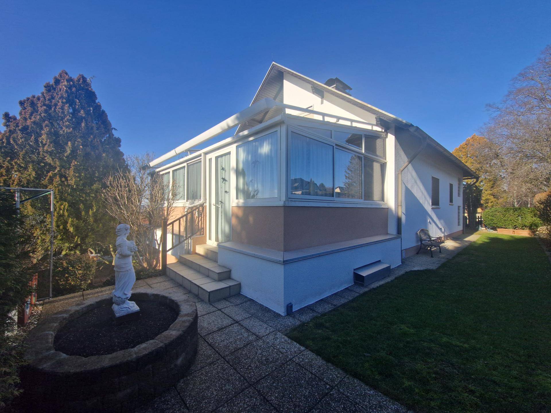Seitenansicht des Hauses mit Wintergarten, gepflasterter Terrasse und Garten.