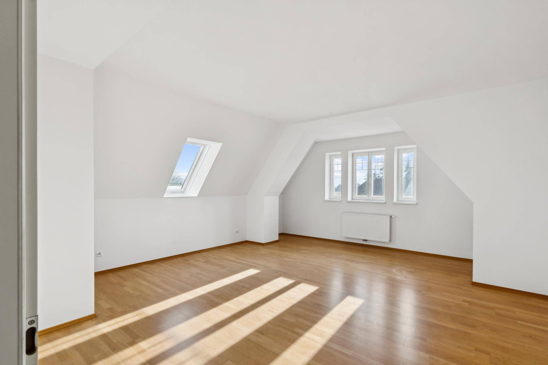 Lichtdurchflutetes Dachzimmer mit Holzboden und mehreren Fenstern, die eine weite Aussicht bieten.