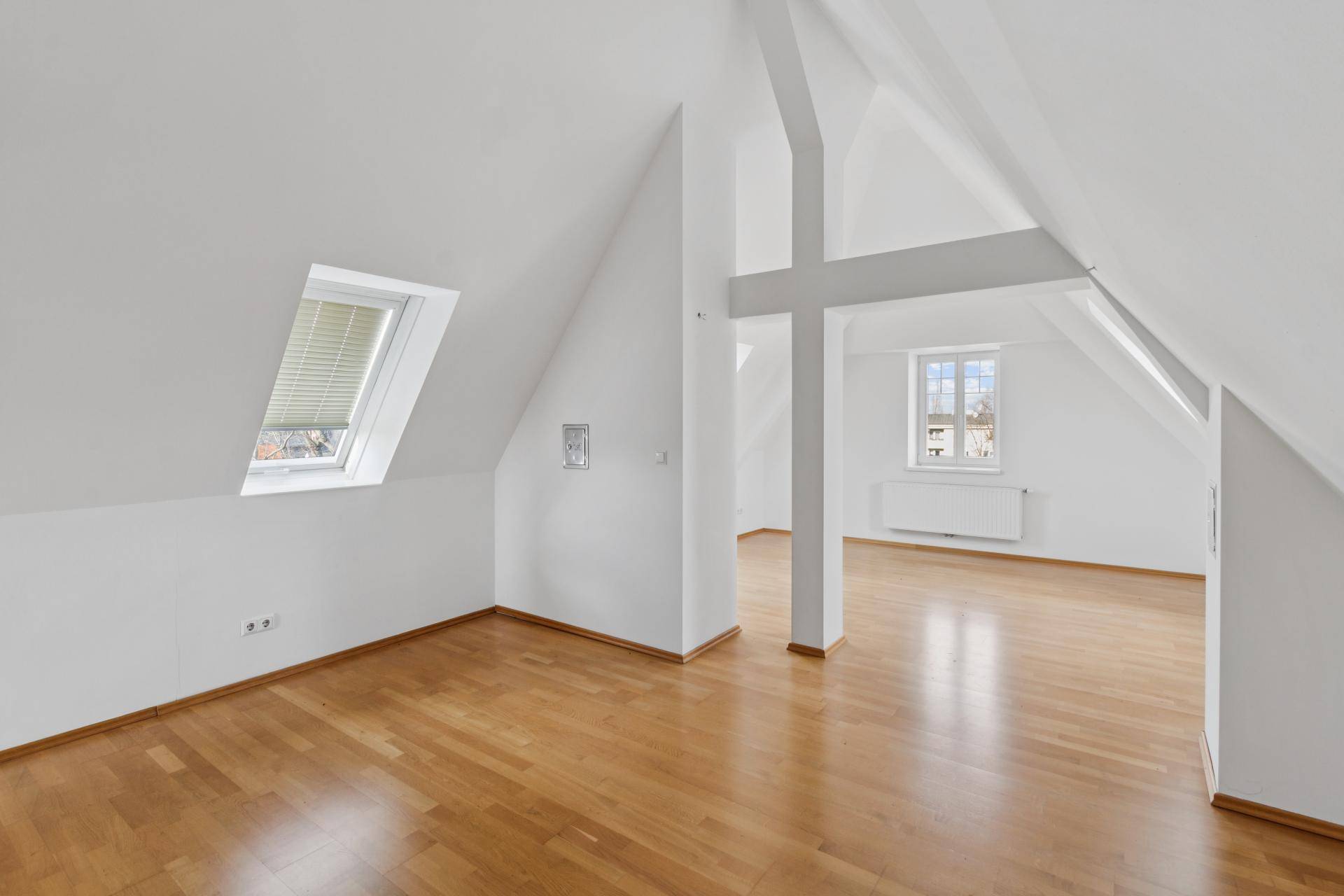 Helles Dachzimmer mit sichtbaren Dachbalken, schrägen Wänden und Holzboden.