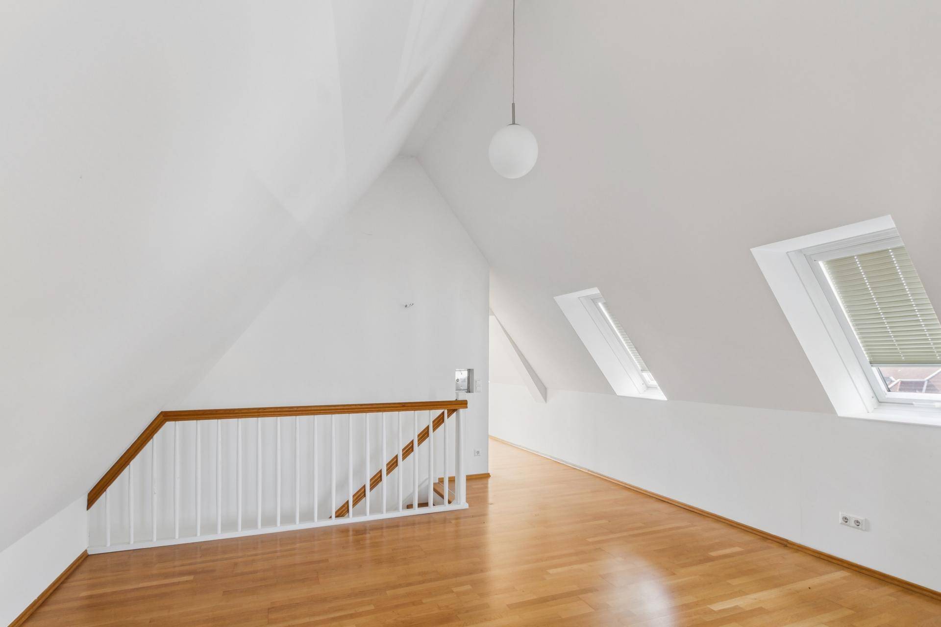 Geräumiges Dachzimmer mit schrägen Wänden, Holzboden und Dachfenstern für natürliches Licht.