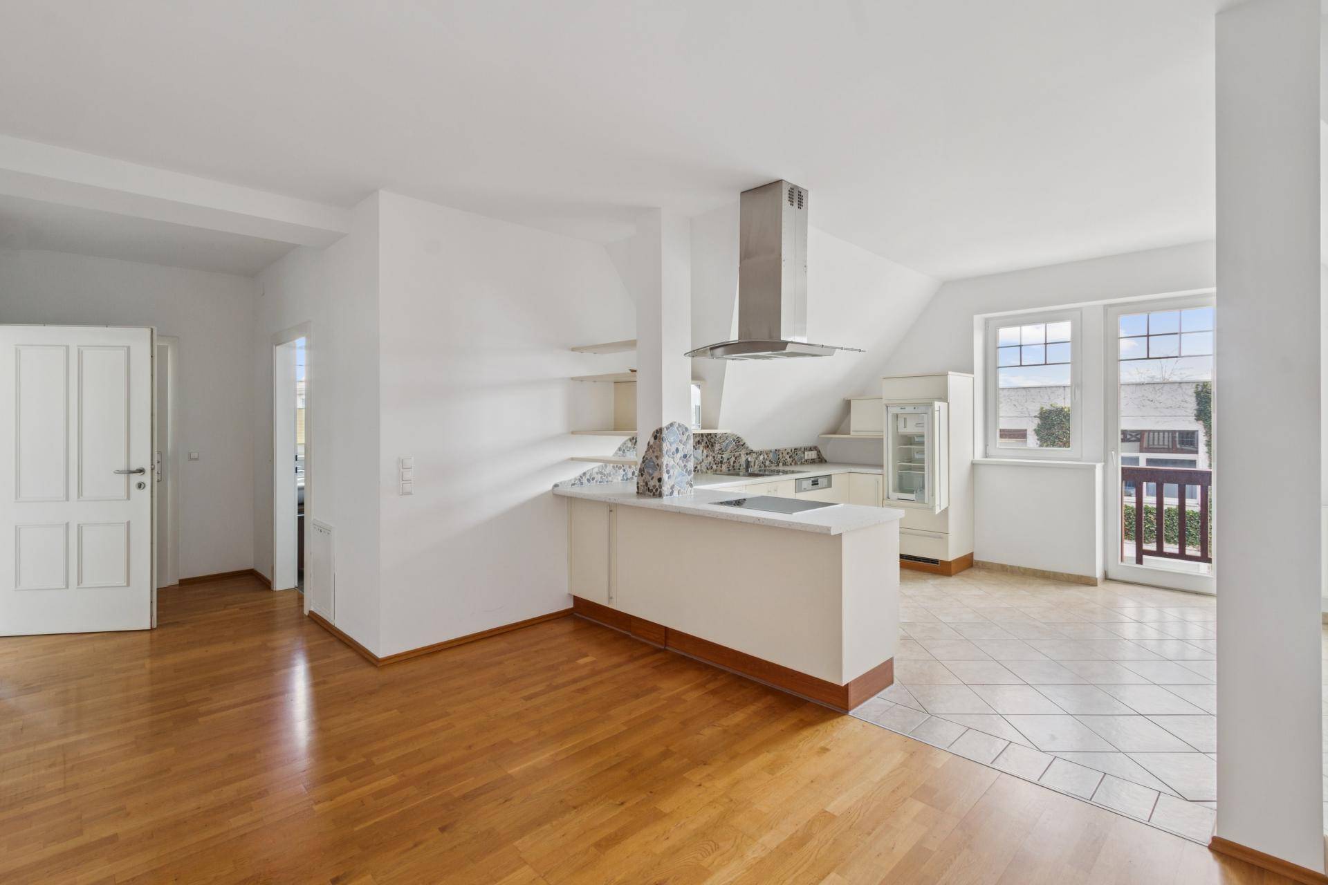 Offene Küche mit Kochinsel, Dunstabzugshaube und Zugang zu einem kleinen Balkon.