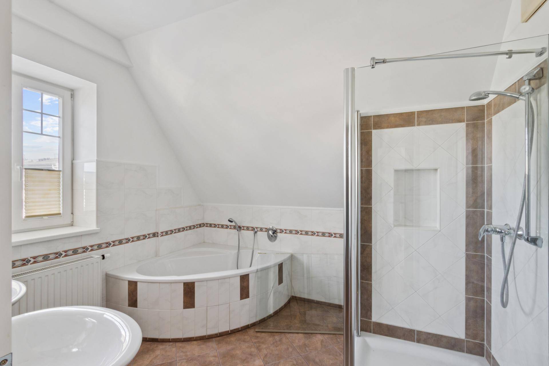 Badezimmer mit Eckbadewanne, Duschkabine und hellen Fliesen in Braun- und Weißtönen.