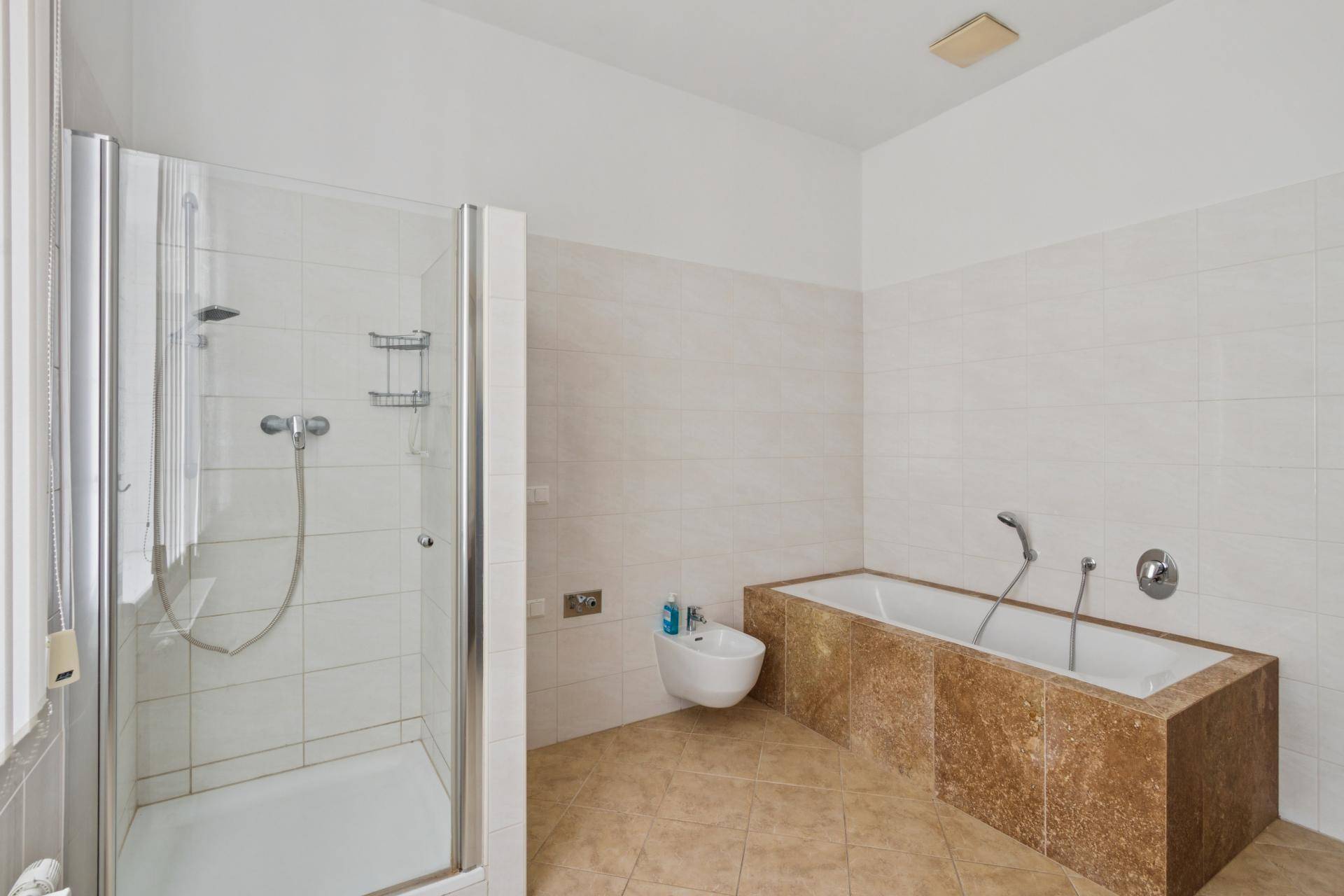 Geräumiges Badezimmer mit Badewanne, Duschkabine, Bidet und beigefarbenen Fliesen.