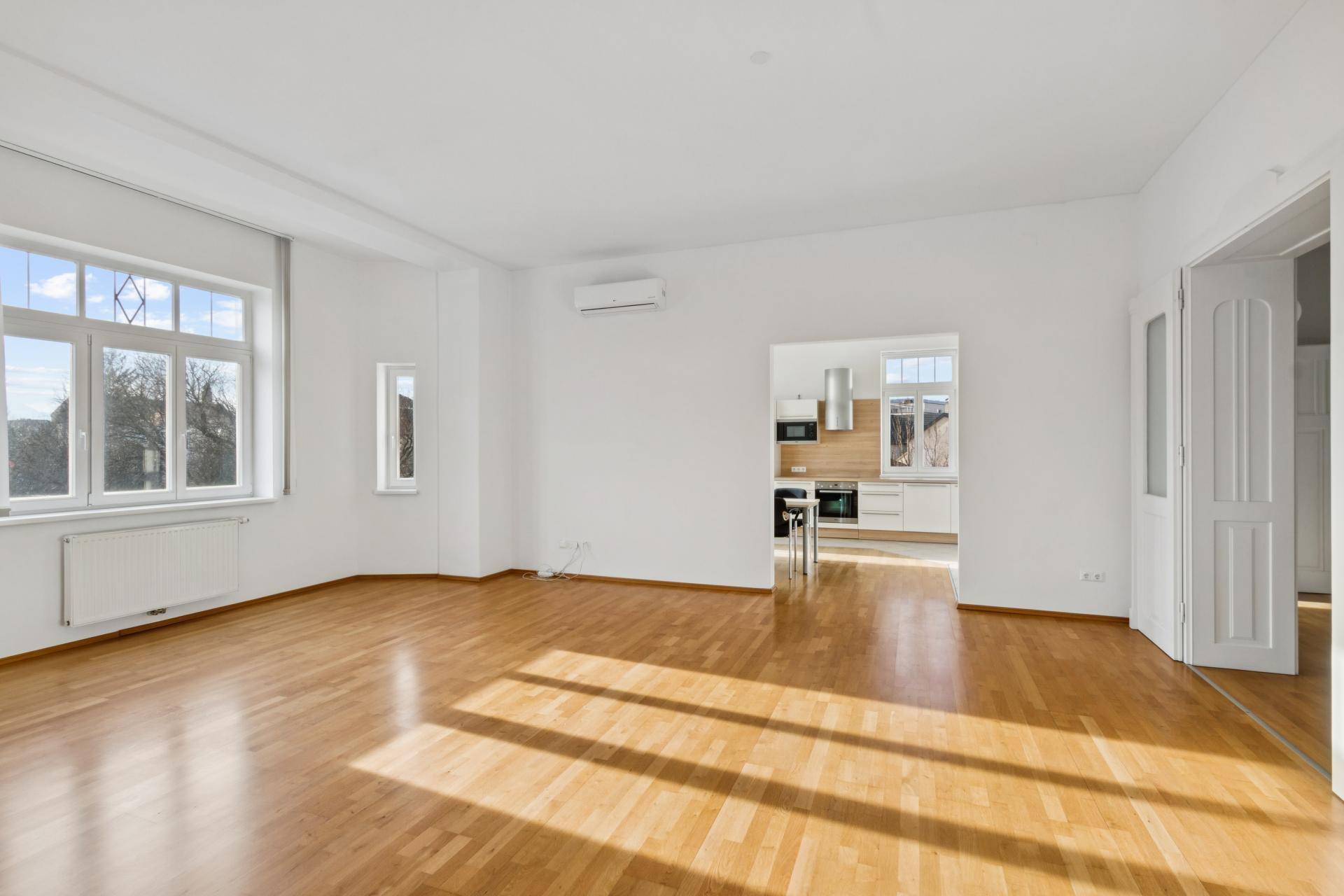 Geräumiges Wohnzimmer mit Parkettboden und offenem Zugang zu einer modernen Küche.