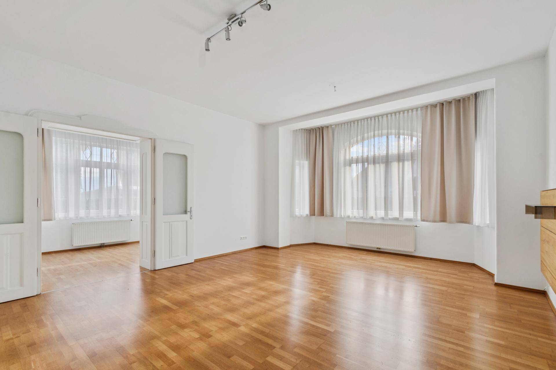 Helles Wohnzimmer mit Parkettboden und großen Fenstern, die viel Tageslicht hereinlassen.