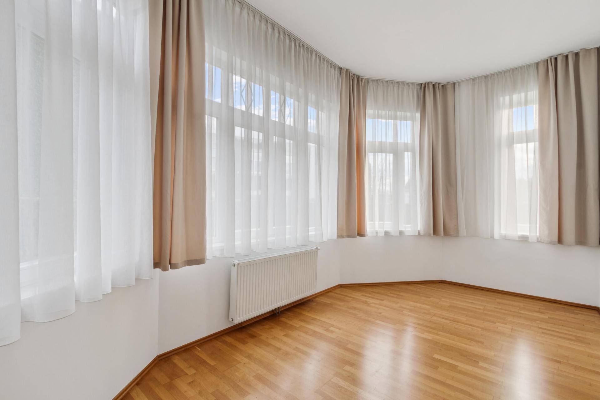 Heller Raum mit Parkettboden und einem Erkerfenster, das den Raum mit Licht füllt.