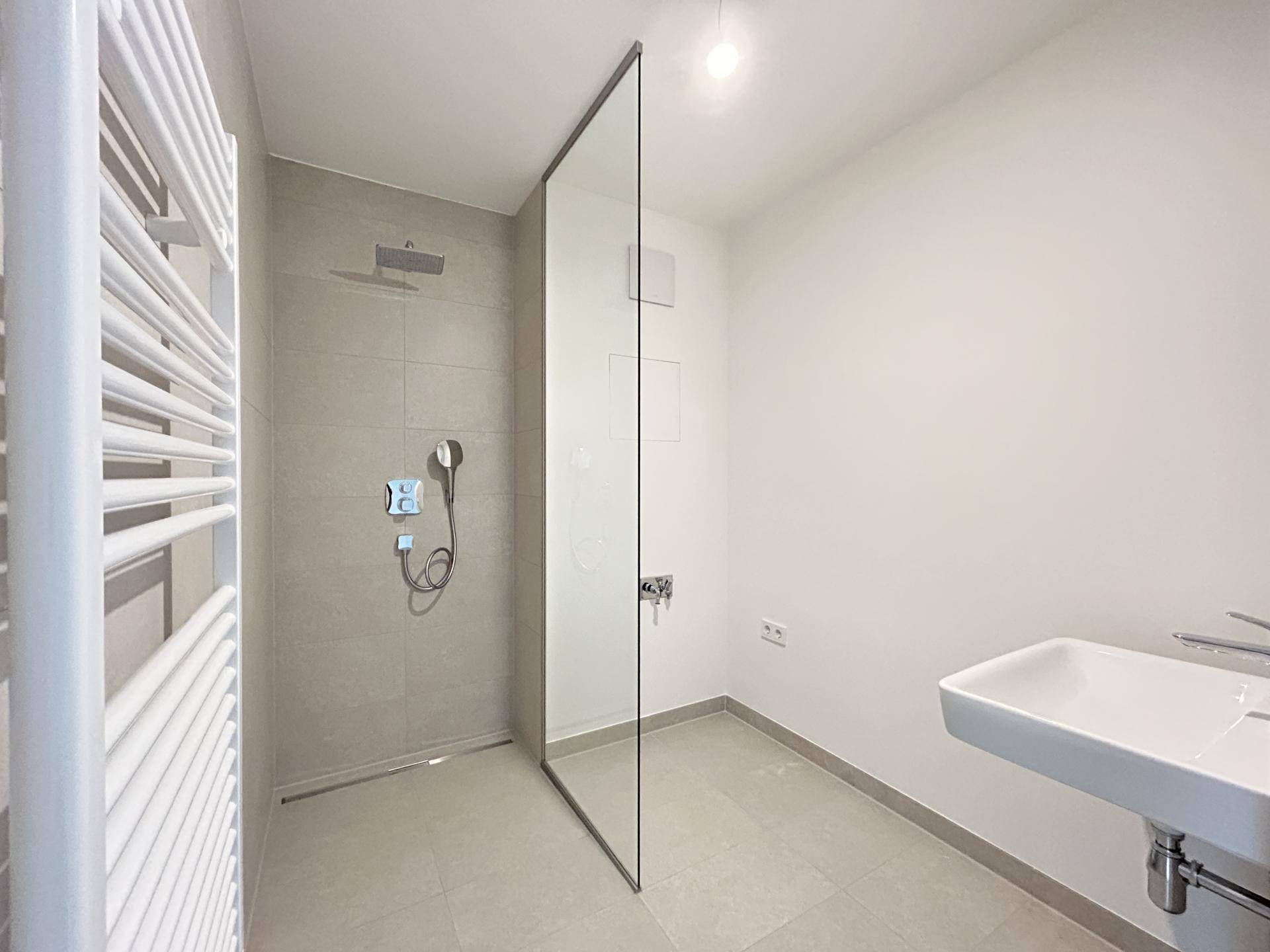 Modernes Badezimmer mit ebenerdiger Dusche, Glaswand und beheiztem Handtuchhalter.