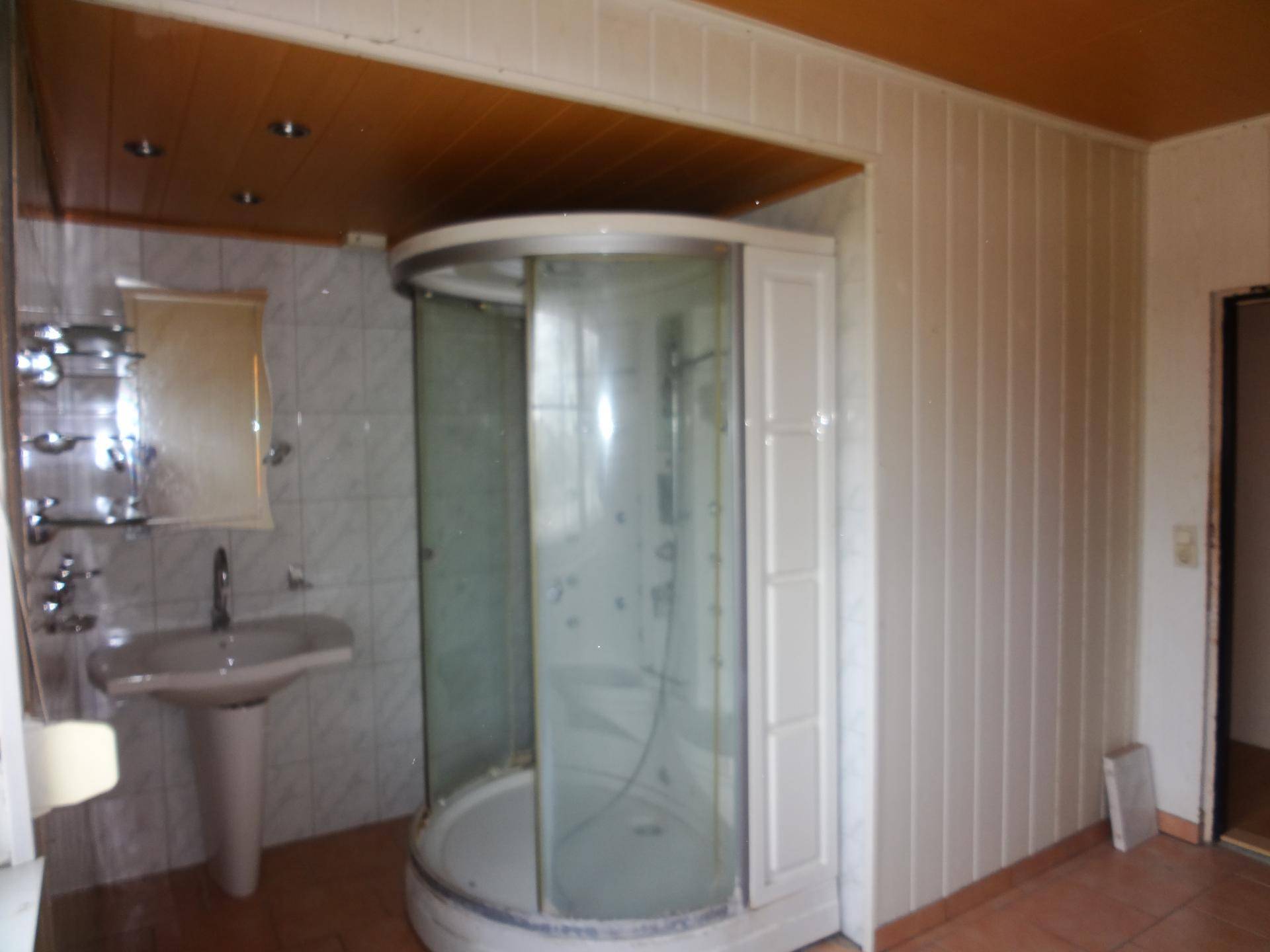 Badezimmer mit runder Duschkabine, Standwaschbecken und gefliesten Wänden, in originalem Zustand.