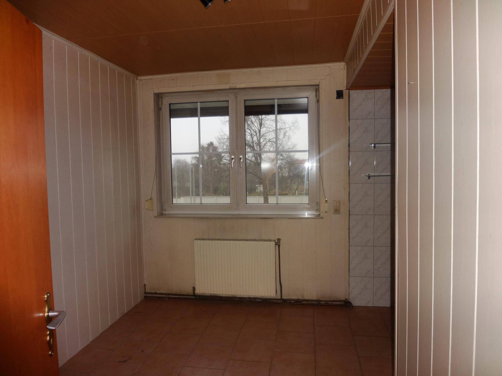Raum mit Holzpaneeldecke, Fliesenboden und einem Fenster, das Tageslicht hereinlässt, in originalem Zustand.
