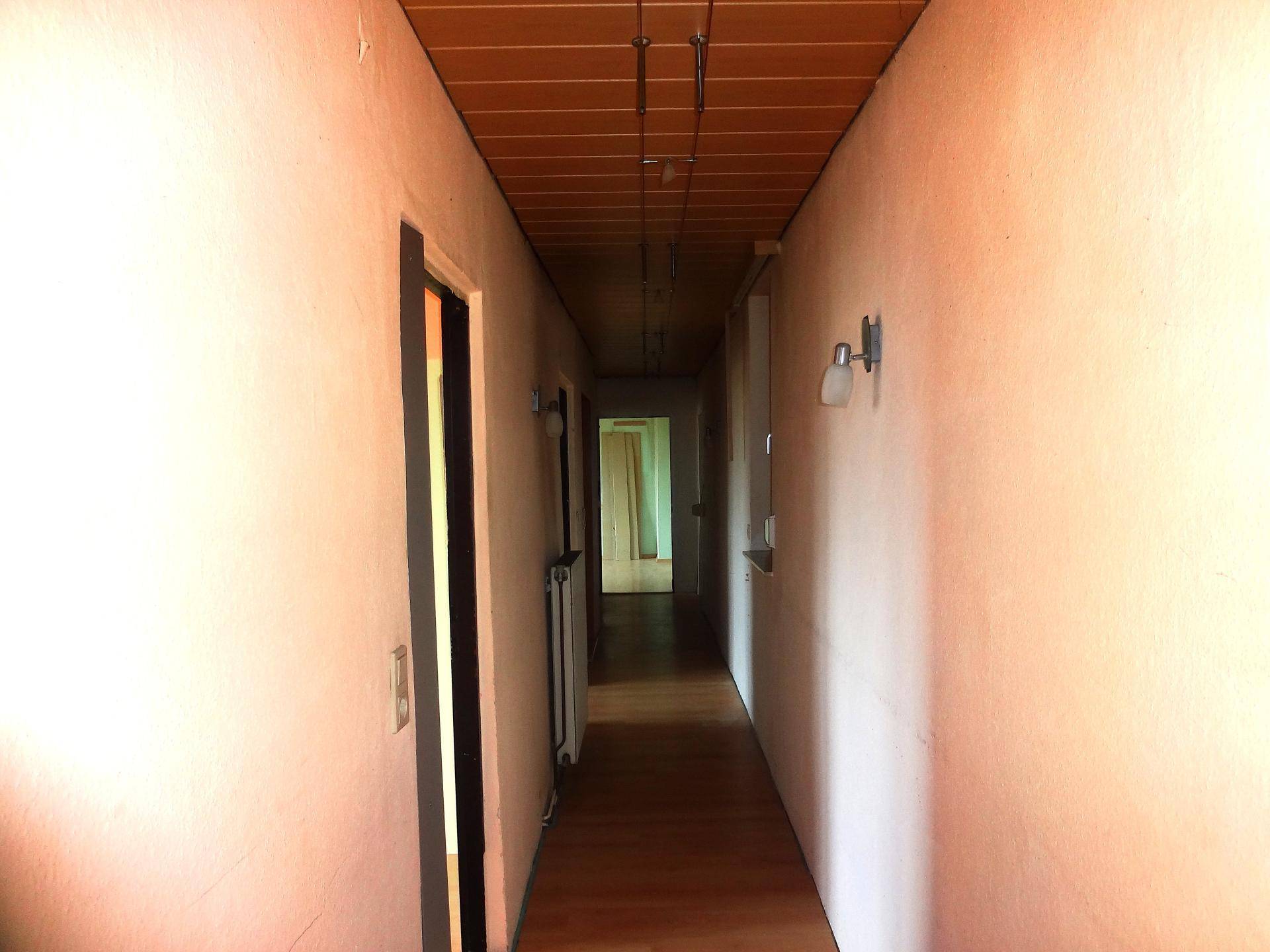 Schmaler Flur mit Holzpaneeldecke und Holzboden, der zu weiteren Räumen im Haus führt.