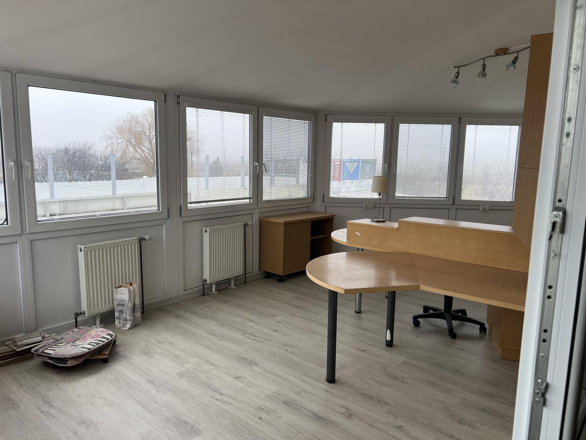Helles Büro mit großen Fenstern, Jalousien und einem funktionalen Schreibtischbereich mit Laminatboden.