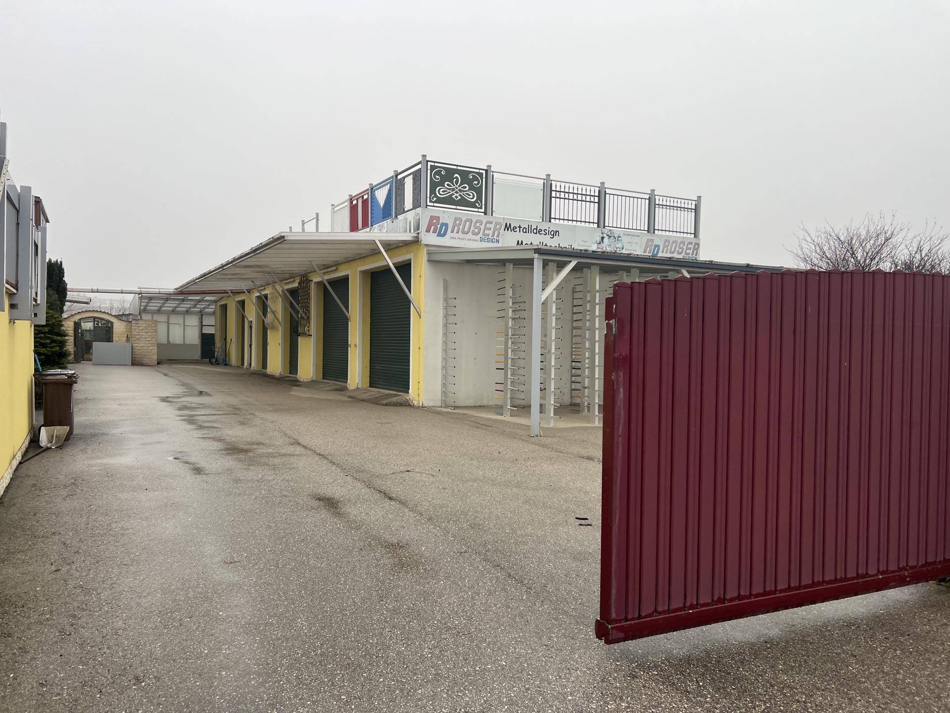 Weitläufiger Außenbereich mit einer langen Zufahrt, Garagenreihen und einem roten Schiebetor.