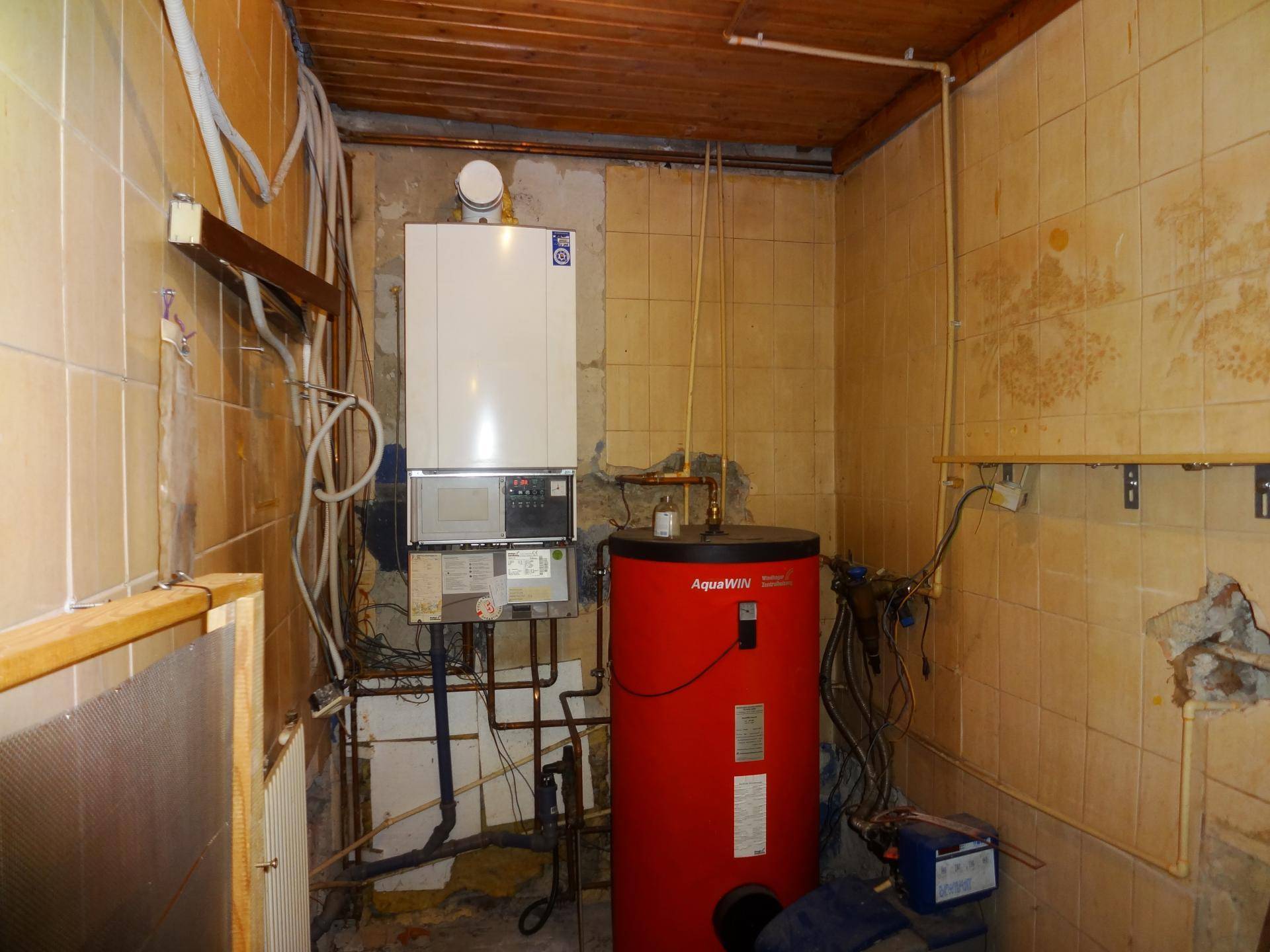 Heizungsraum mit einem Boiler und sichtbaren Rohrleitungen, gefliesten Wänden und Decke in originalem Zustand.