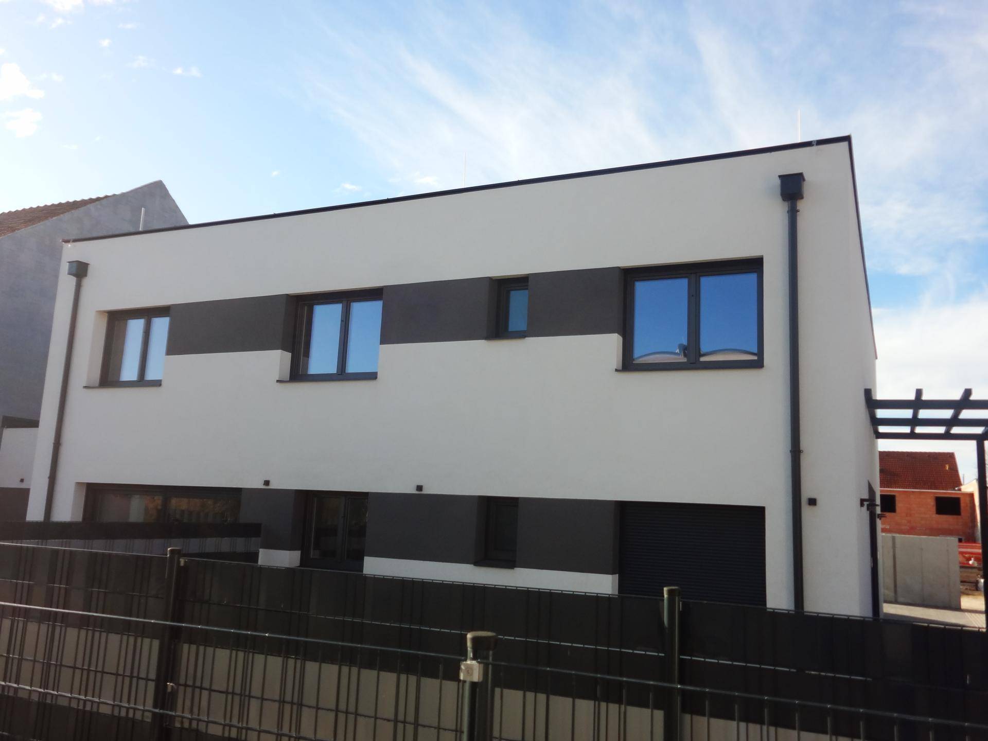 Moderne Fassade eines Neubaus mit großen Fenstern und dunklen Akzenten unter blauem Himmel.