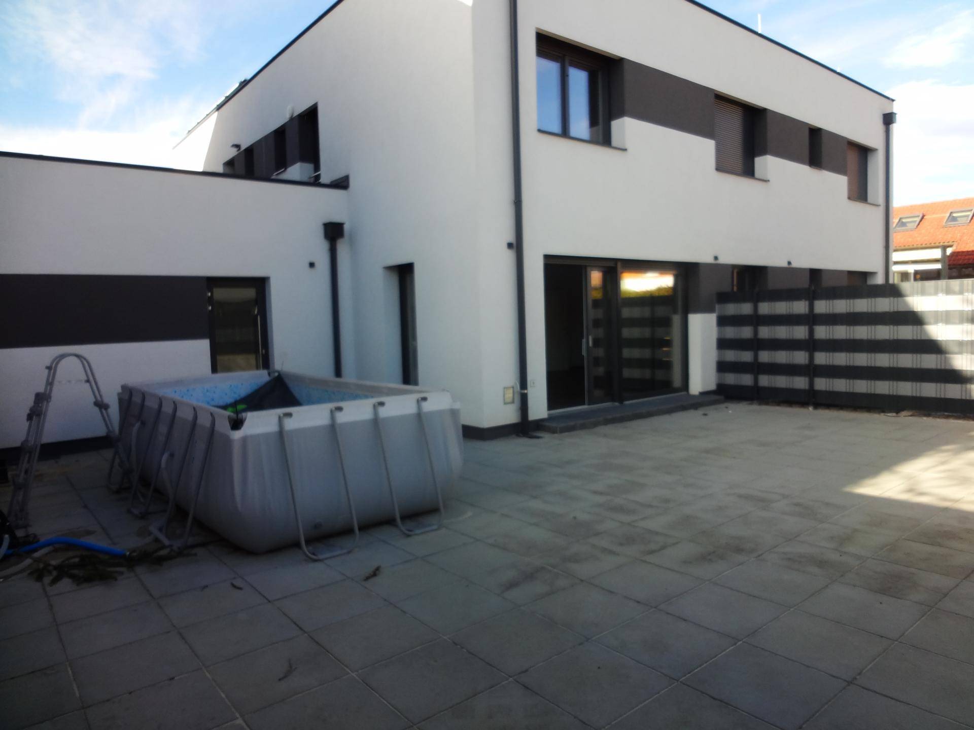 Hinterhofbereich mit gepflasterter Terrasse und einem temporären Aufstellpool neben dem modernen Gebäude.