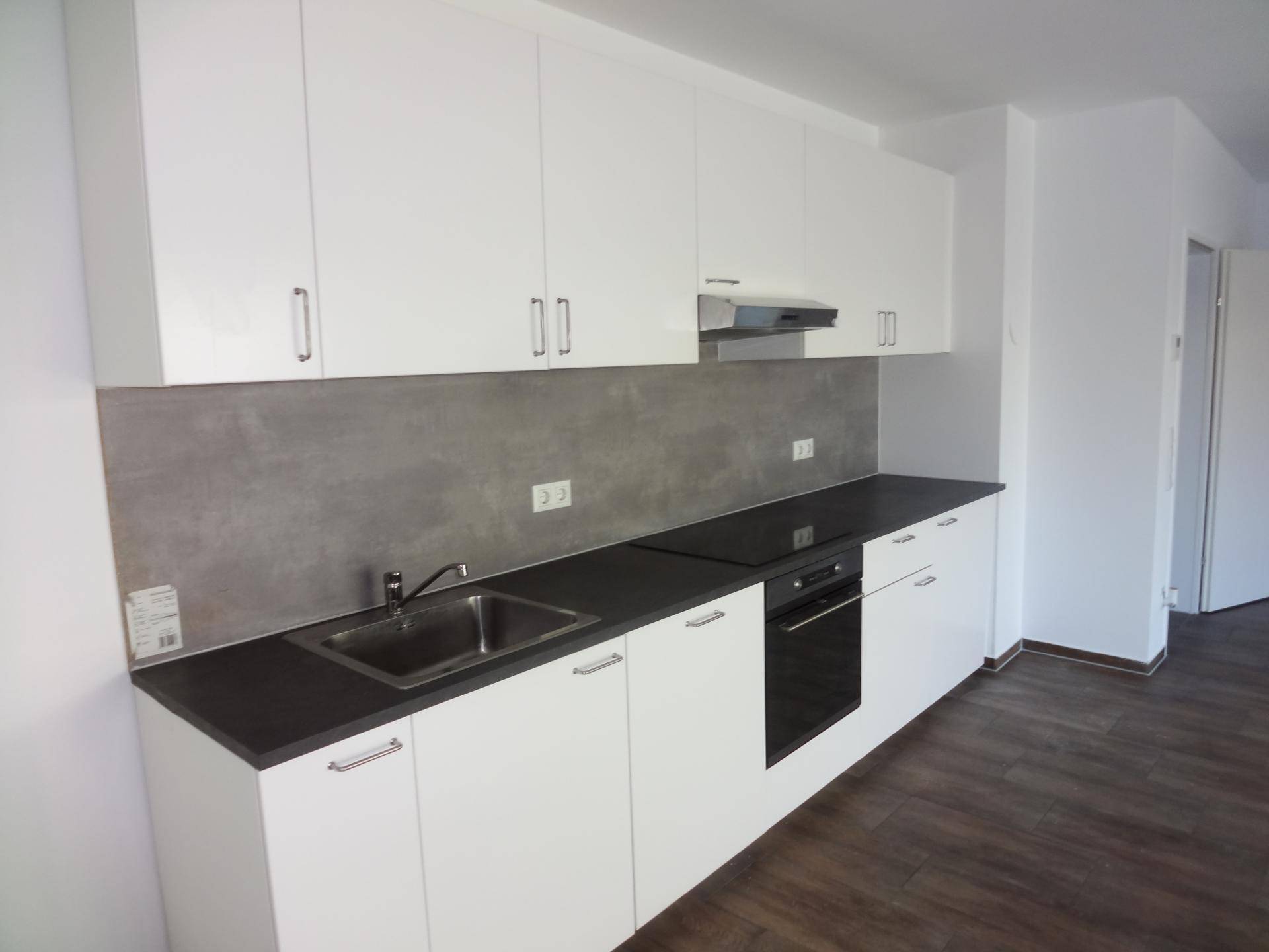 Moderne Einbauküche mit weißen Schränken, dunkler Arbeitsplatte und integrierten Geräten.