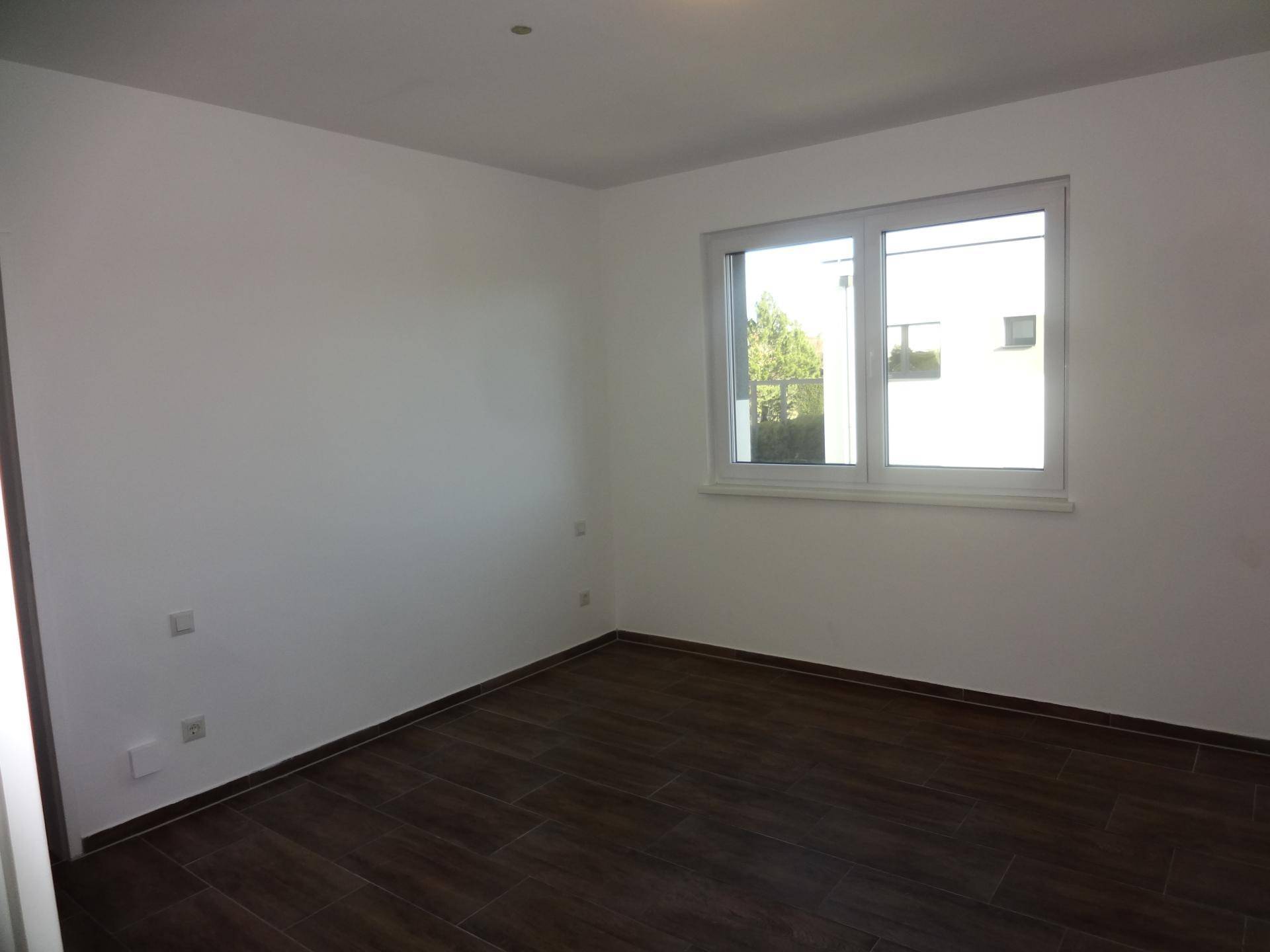 Helles Zimmer mit großem Fenster und dunklem Fliesenboden, ideal als Schlaf- oder Arbeitszimmer.