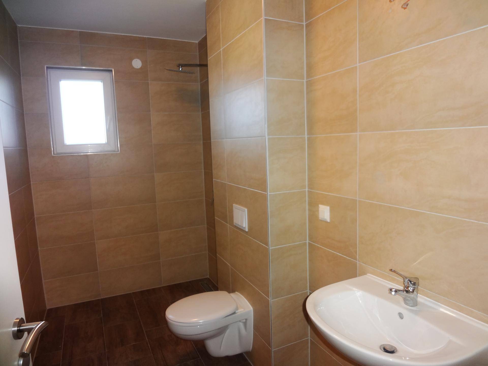 Modernes Badezimmer mit beigefarbenen Fliesen, wandhängendem WC, Waschbecken und Duschbereich.