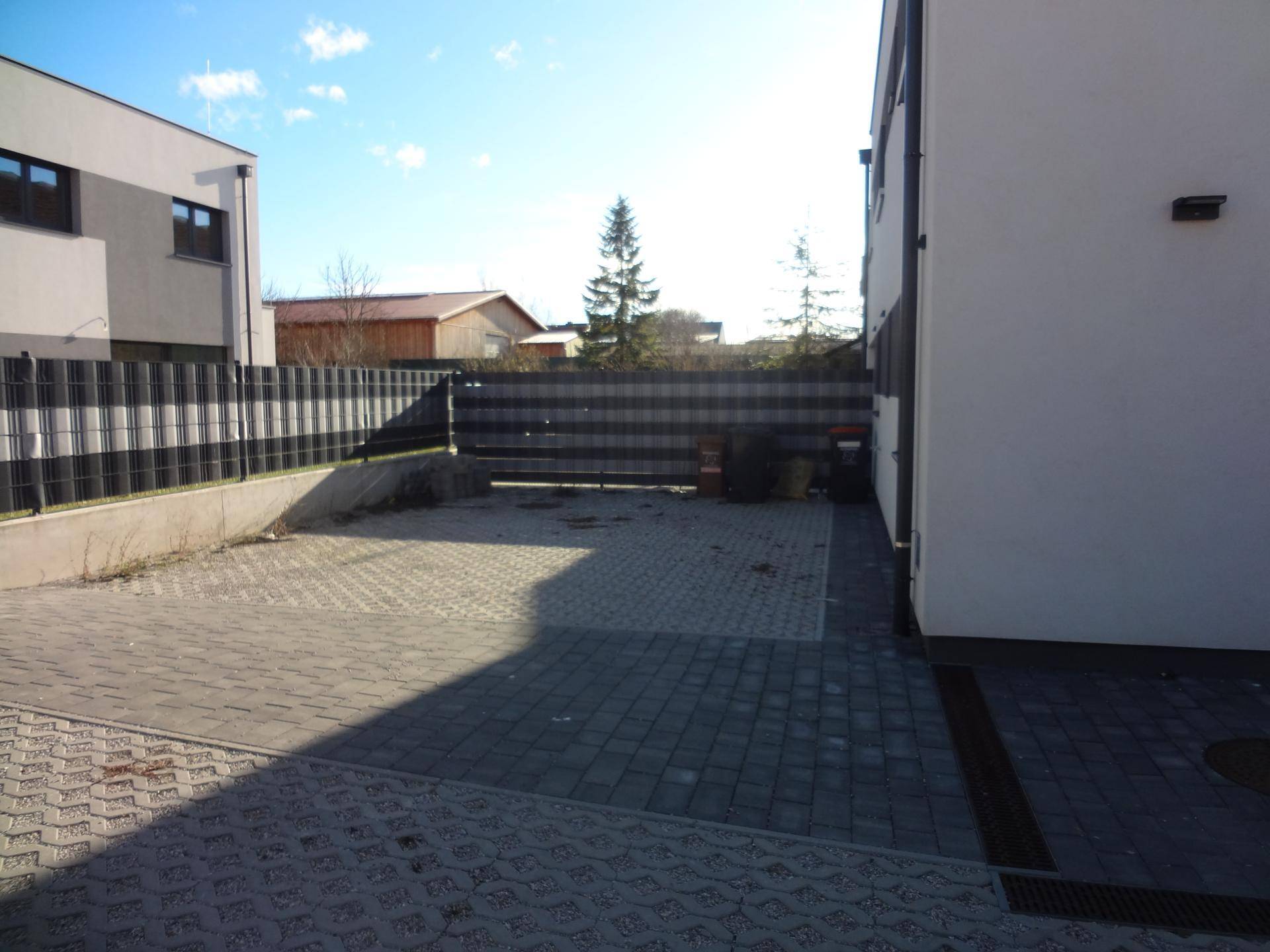 Gepflasterter Außenbereich mit Parkmöglichkeiten und Zaun, angrenzend an das Gebäude.