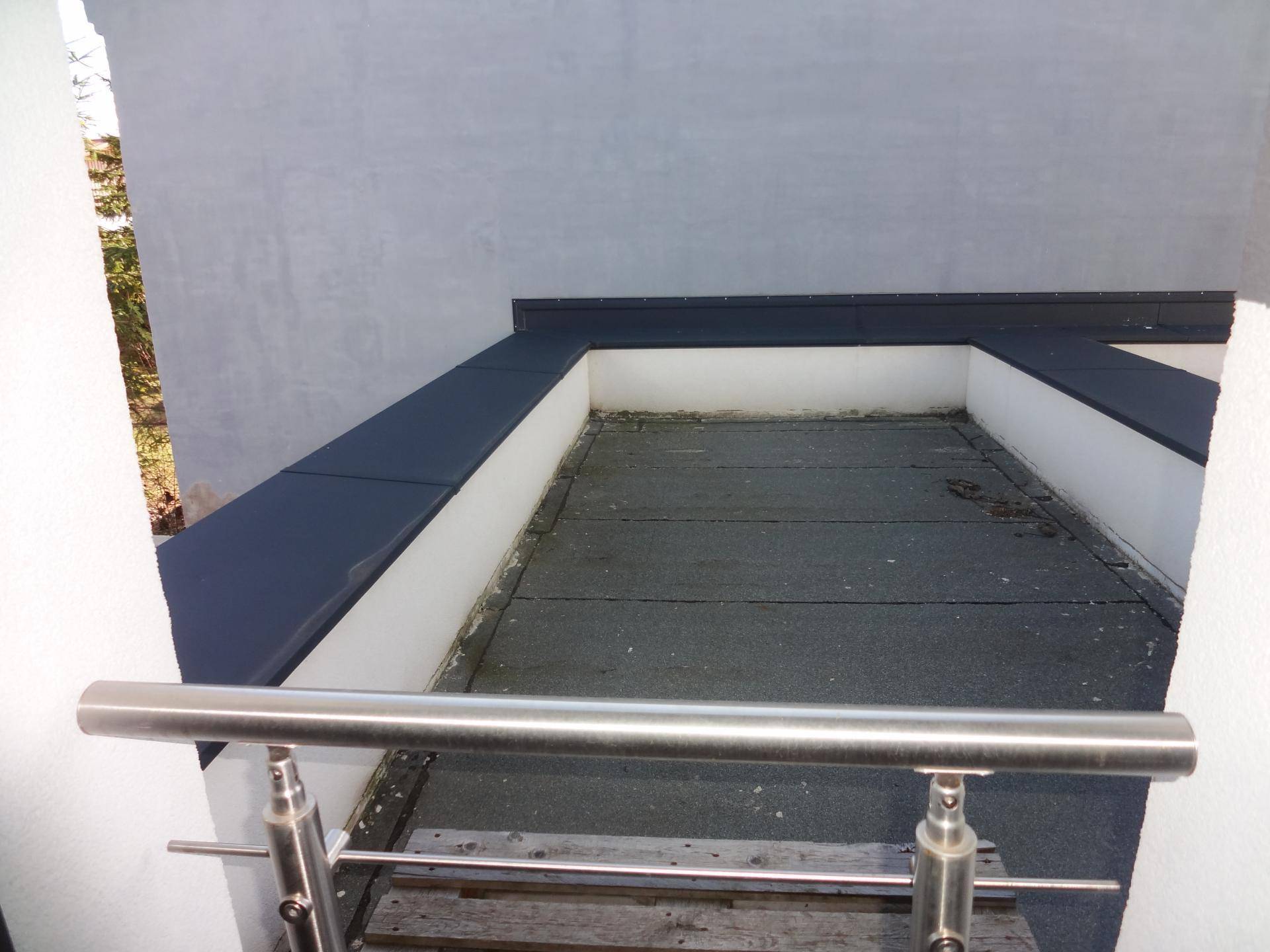 Kleiner, ummauerter Außenbereich mit Metallgeländer, möglicherweise ein Balkon oder eine Dachterrasse.