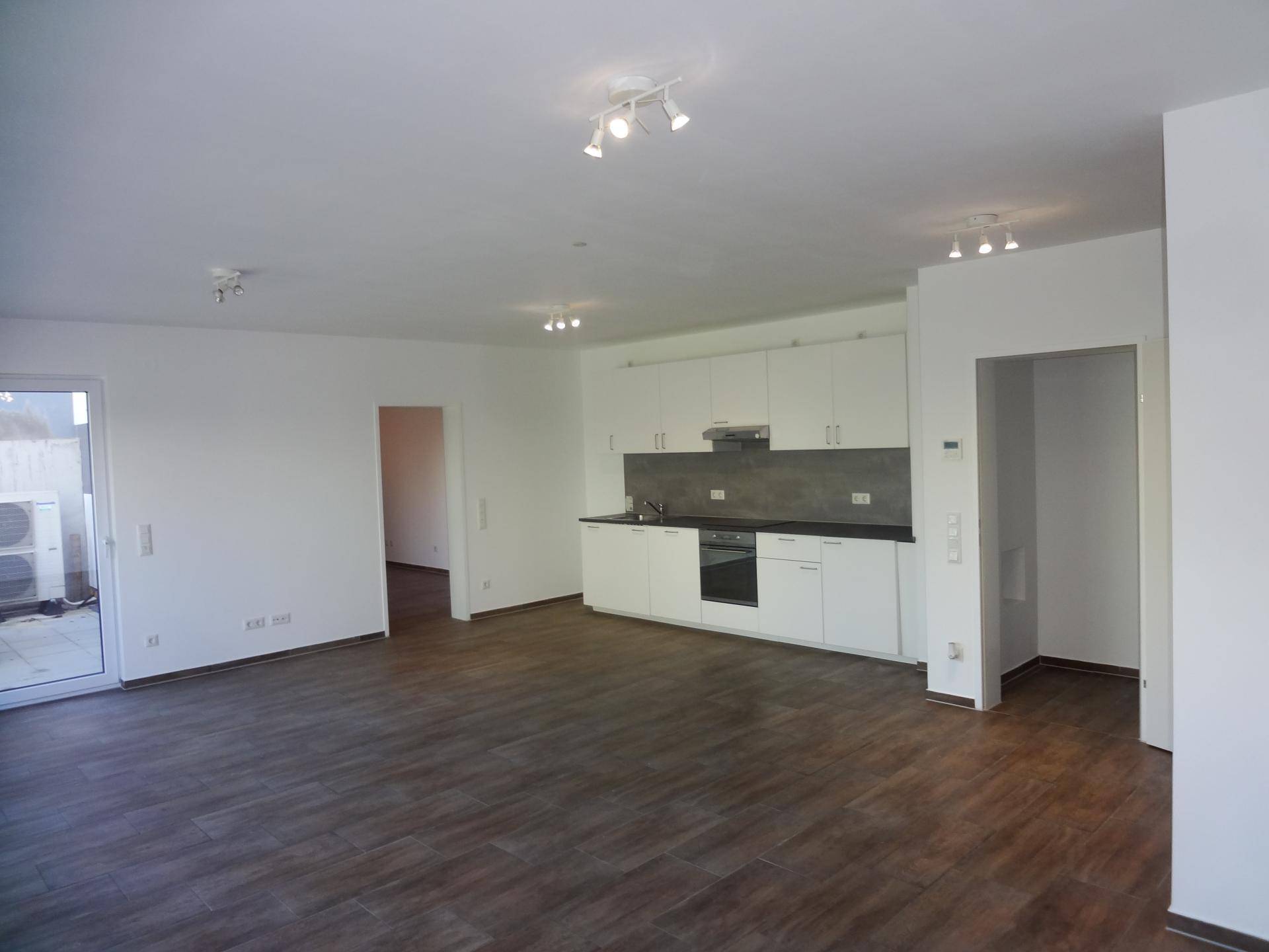 Offener Wohnbereich mit integrierter Küche, dunklem Fliesenboden und Zugang zur Terrasse.