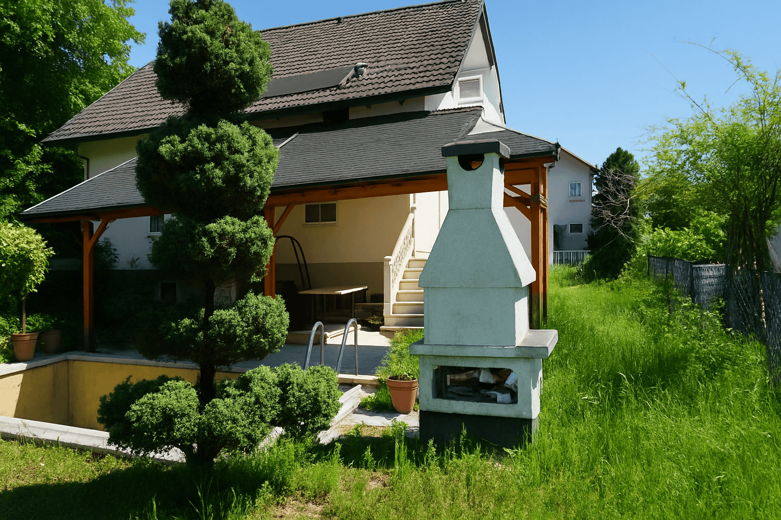 Großer Garten mit Pool, Grillplatz und viel Grünfläche unter blauem Himmel.