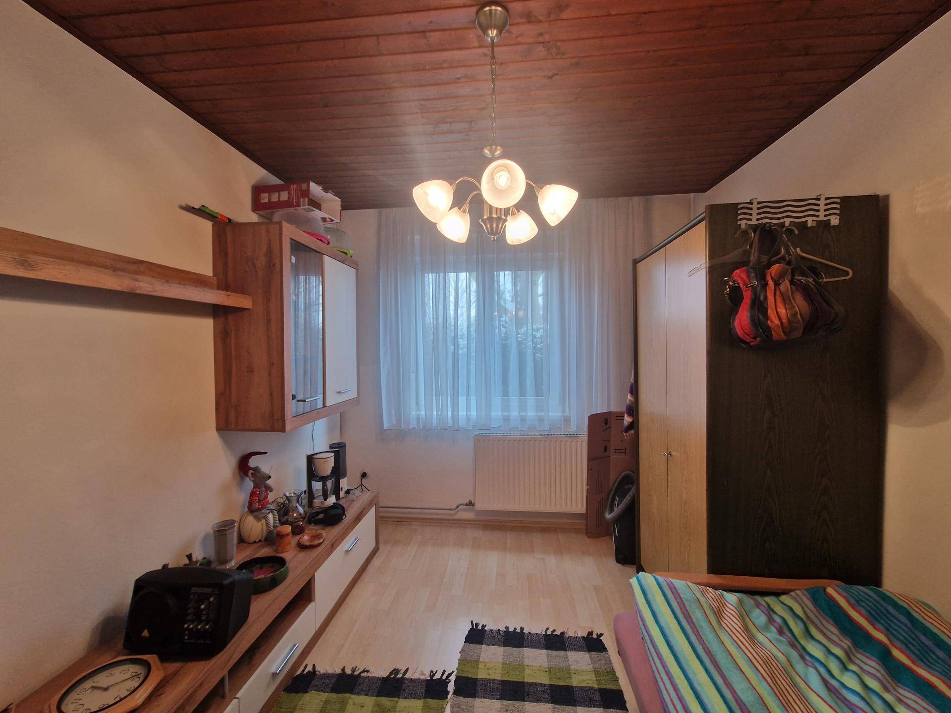 Schlafzimmer mit Holzdeckenverkleidung, hellem Boden und Fenster.