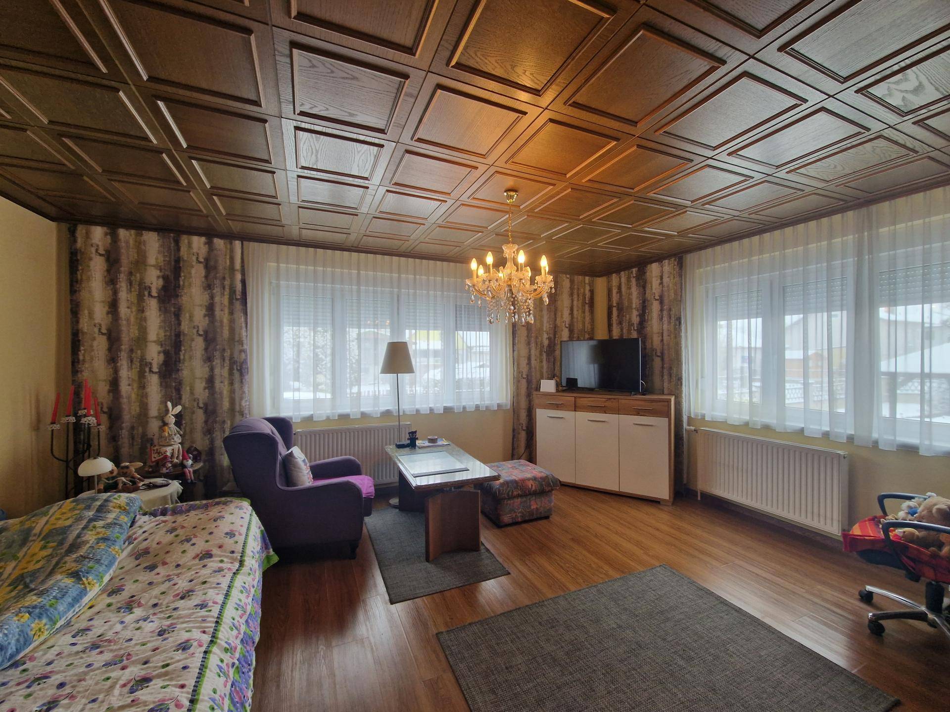 Wohnzimmer mit Holzkassettendecke, Parkettboden und großen Fenstern.