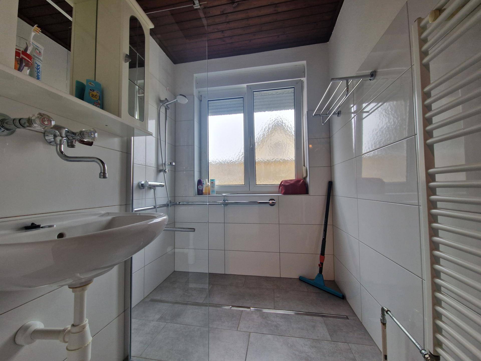 Modernes Badezimmer mit ebenerdiger Dusche, Fenster und Haltegriffen.