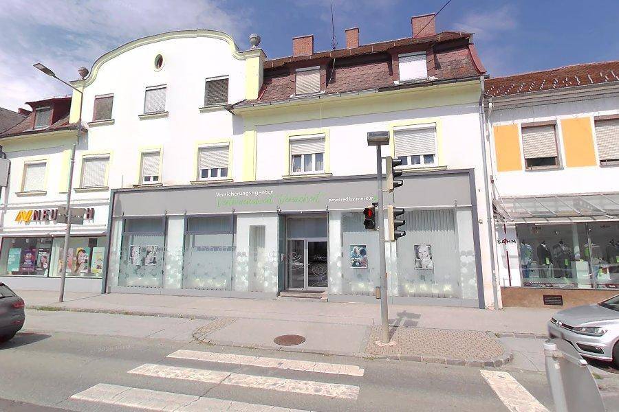 Gebäude mit Geschäftsflächen im Erdgeschoss und Wohnungen in den oberen Etagen, an einer städtischen Straße gelegen.