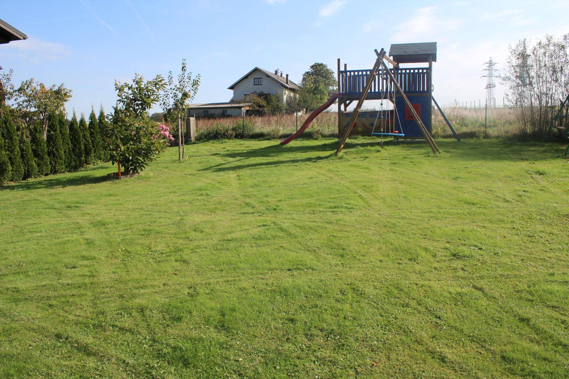 Großer Garten mit Rasenfläche und einem Spielplatz für Kinder.