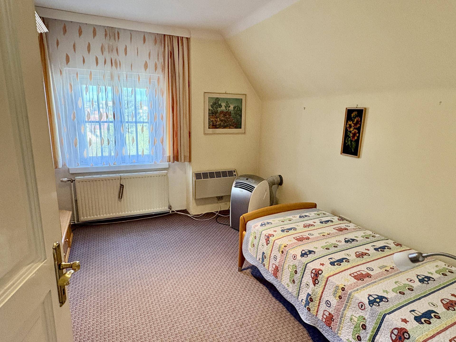 Kinderzimmer mit Teppichboden, einem Einzelbett und einem Fenster, das viel Tageslicht hereinlässt und eine helle Atmosphäre schafft.