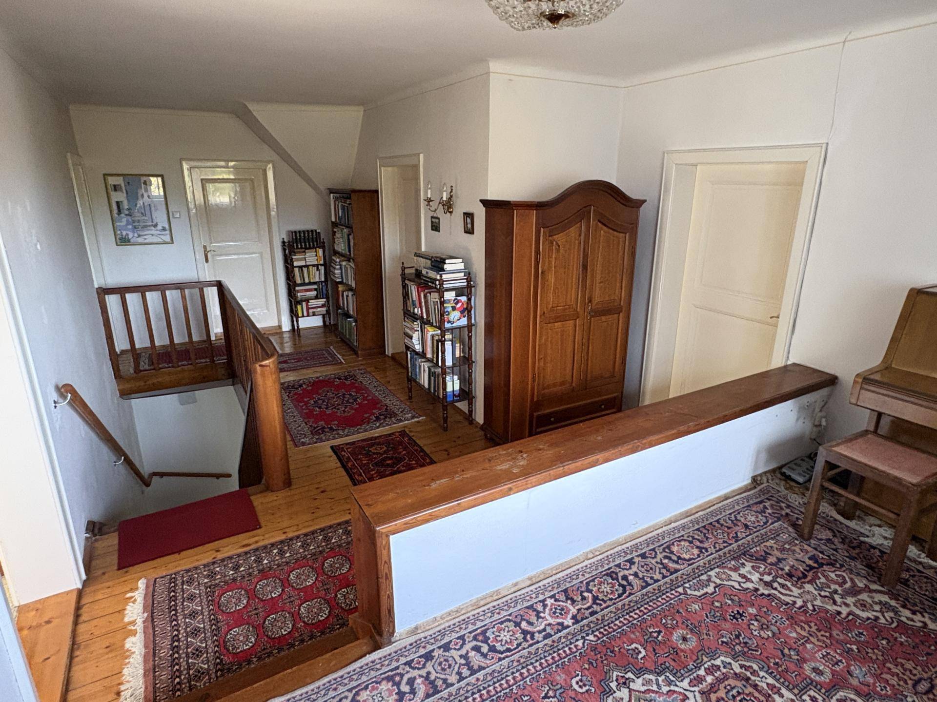 Geräumiger Flur im Obergeschoss mit Holztreppe, Bücherregalen und traditionellen Teppichen, die den Bereich schmücken.