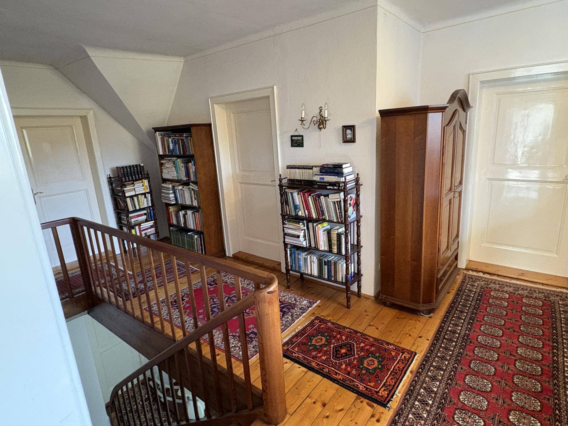 Obergeschoss-Flur mit Holzfußboden, Bücherregalen und traditionellen Teppichen, der zu mehreren Zimmern führt.