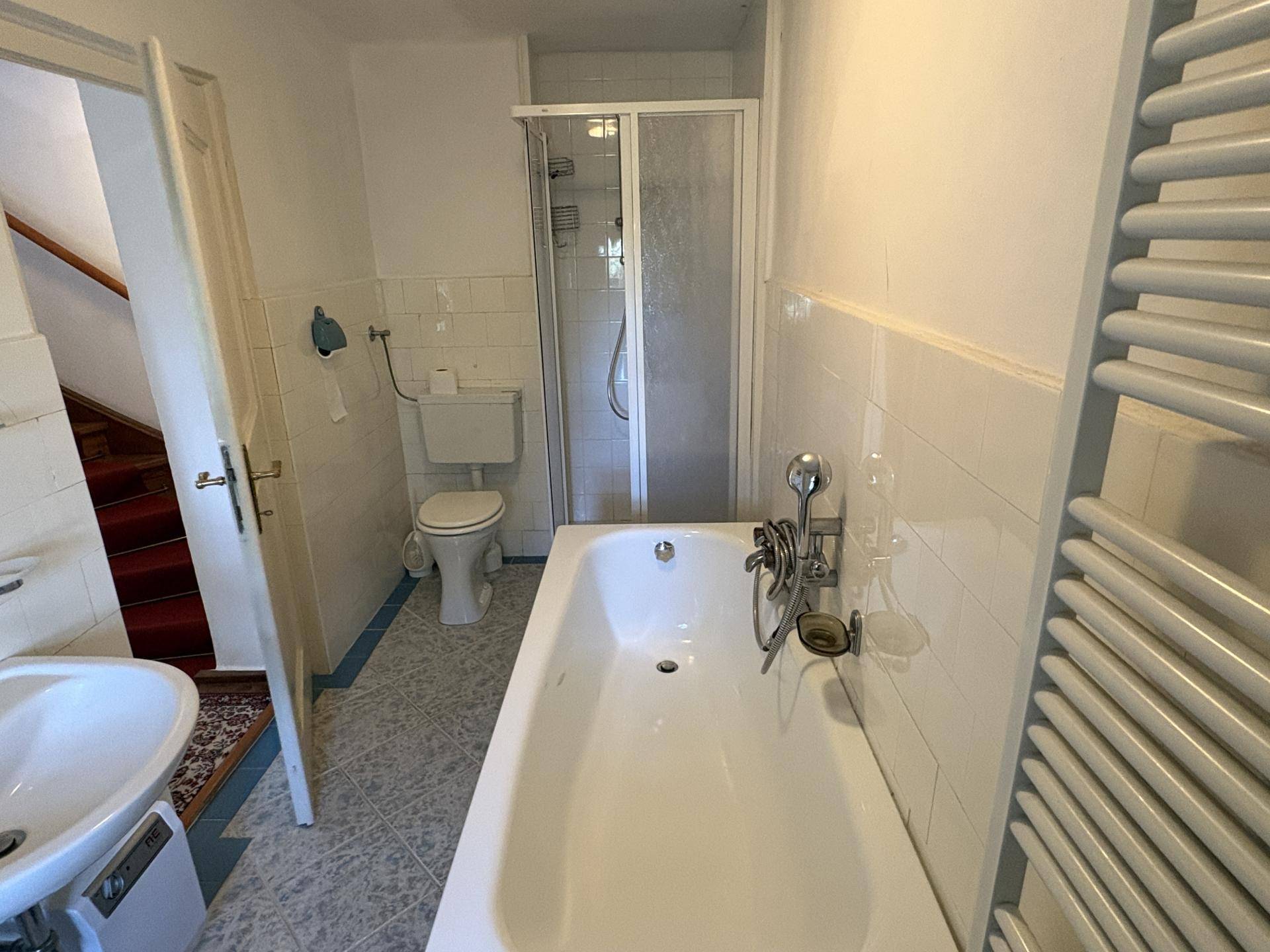 Badezimmer mit Badewanne, Duschkabine, WC und Handtuchheizkörper, gefliest in Weiß und Blau, in gutem Zustand.