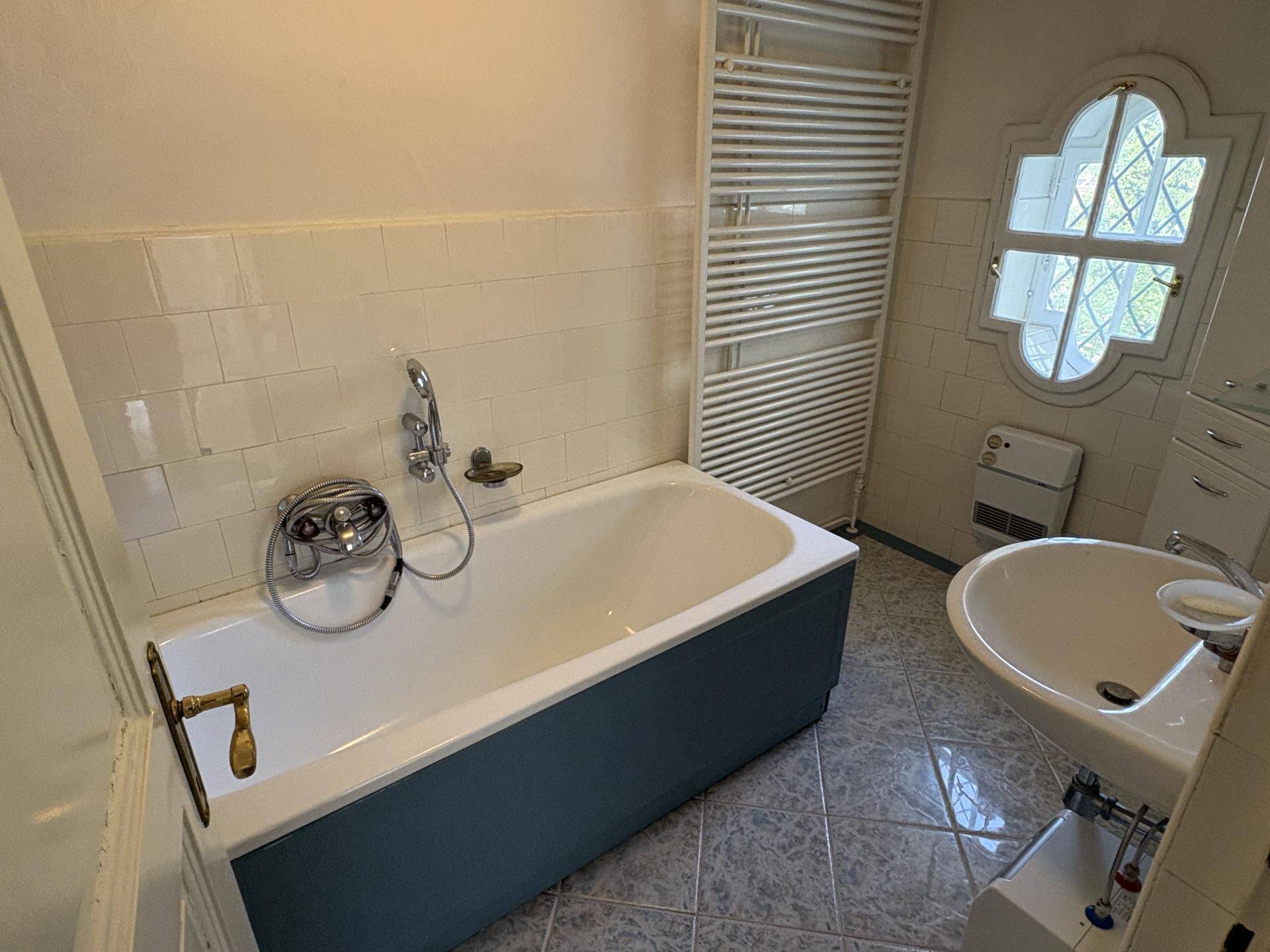 Badezimmer mit Badewanne, Waschbecken und einem dekorativen Fenster, ausgestattet mit einem praktischen Handtuchheizkörper.