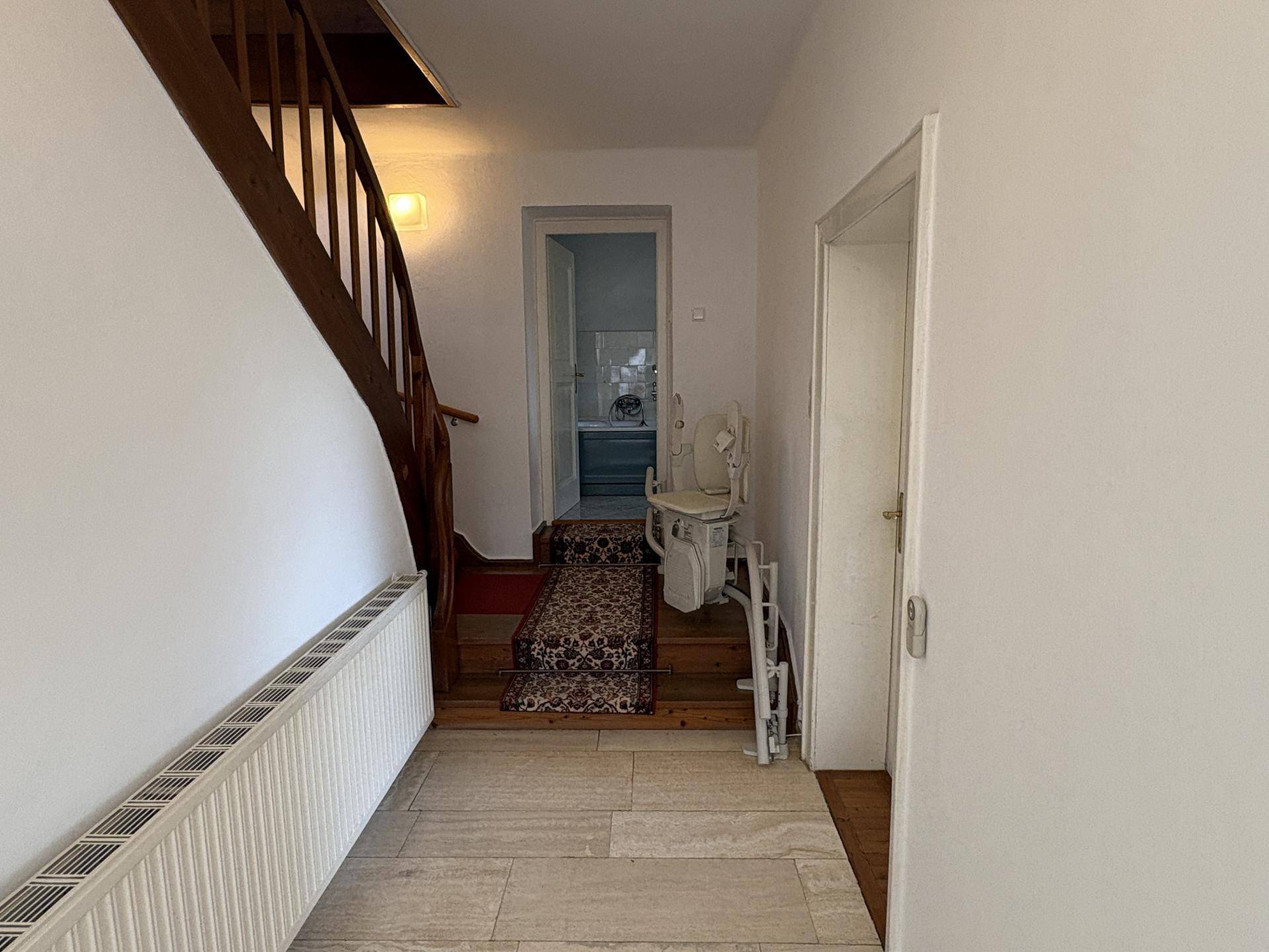 Heller Flur mit Holztreppe, einem Treppenlift und Fliesenboden, der zu weiteren Räumen im Obergeschoss führt.