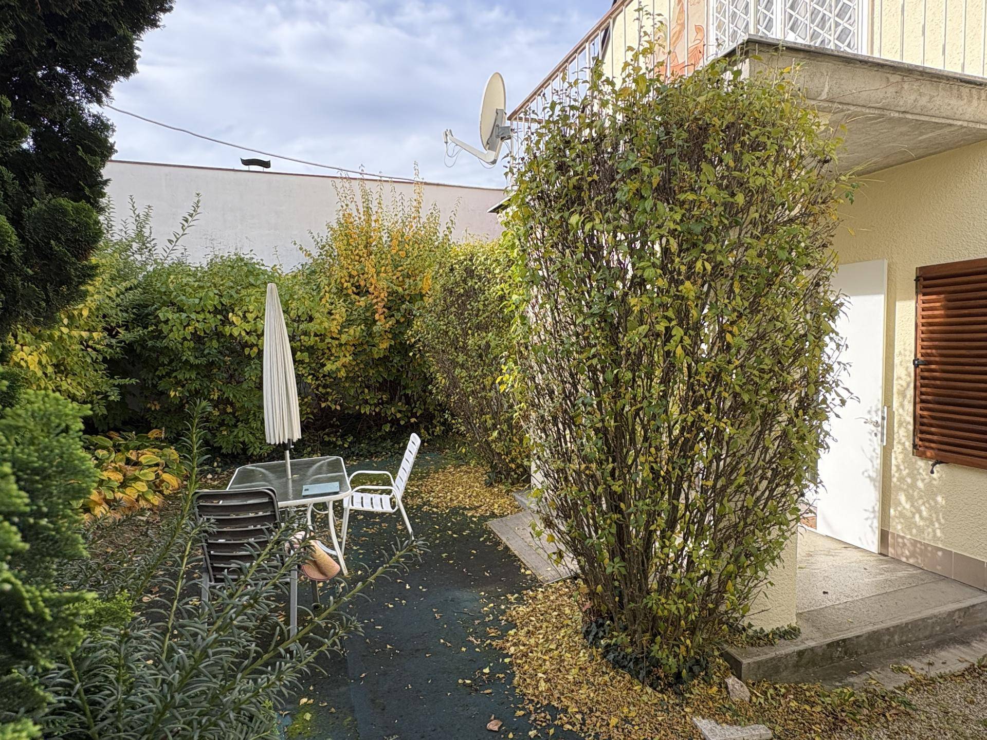 Gartenbereich mit Sitzgelegenheiten, einem Sonnenschirm und üppiger Bepflanzung, ideal zum Entspannen im Freien.