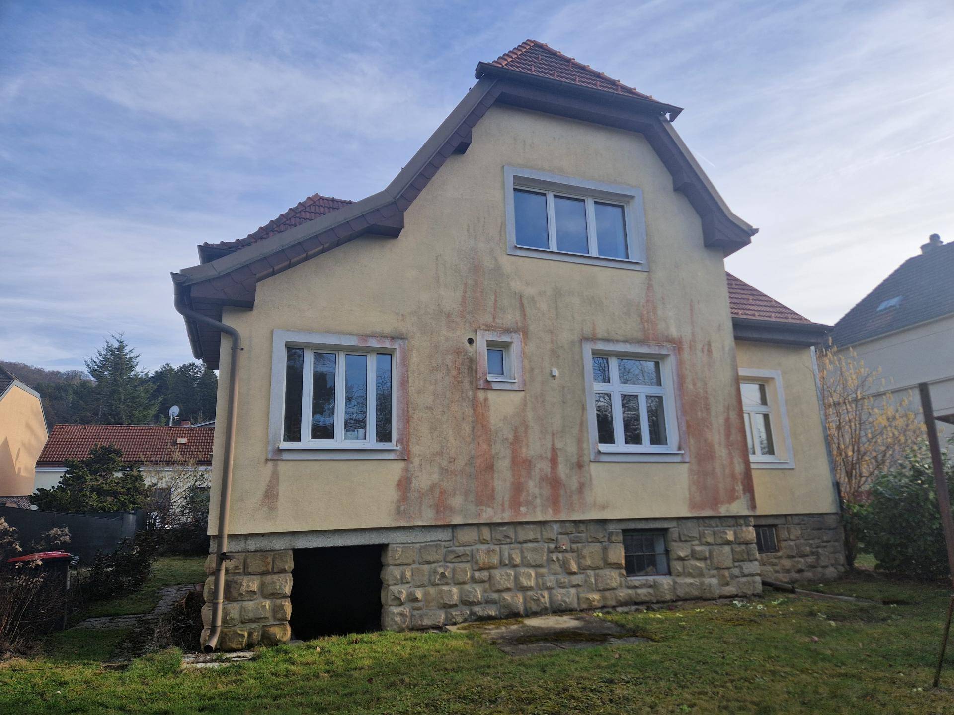 Historisches Einfamilienhaus mit gelber Fassade, Steinsockel und Satteldach in ländlicher Umgebung.