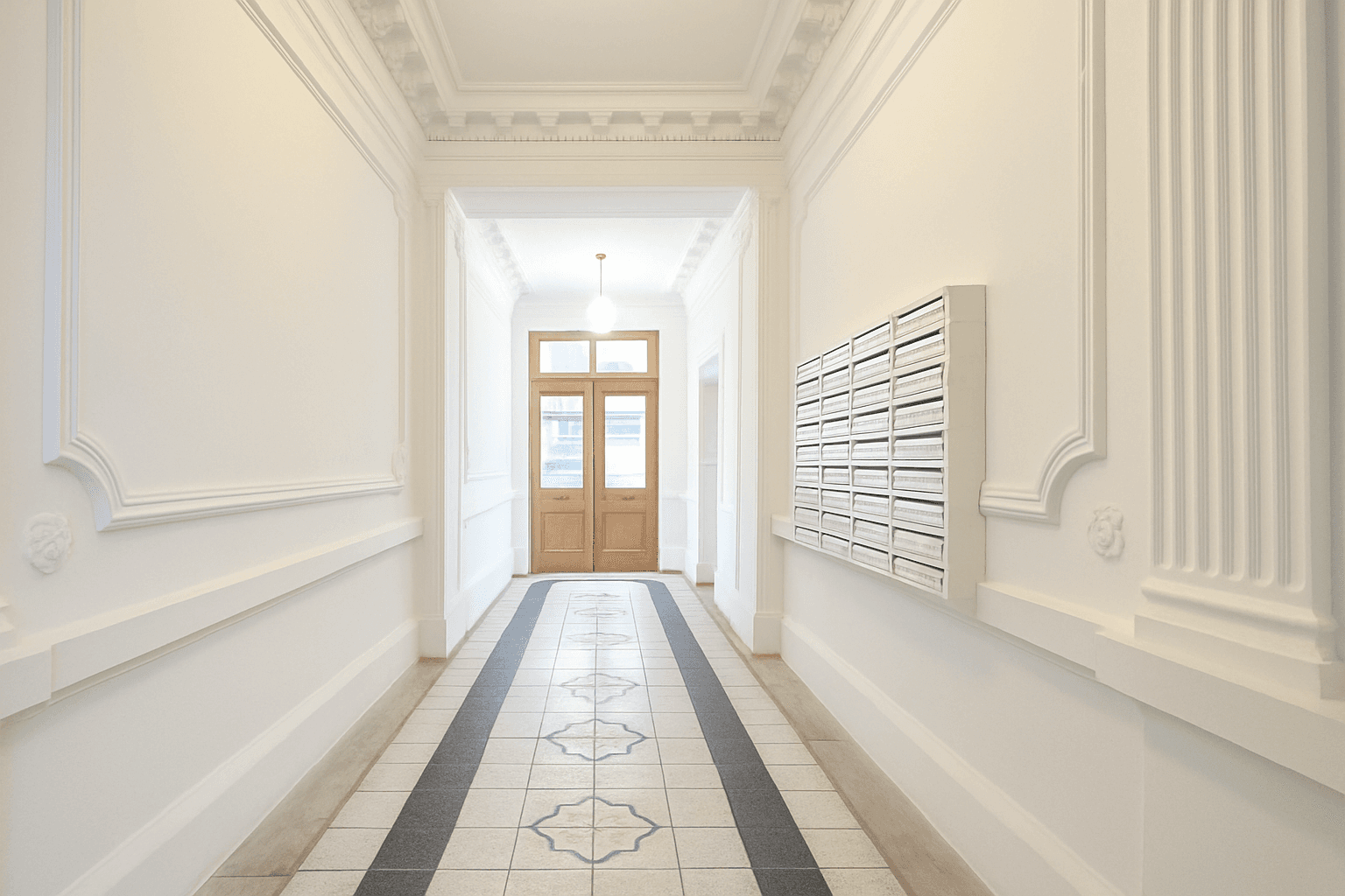 Eleganter Eingangsbereich eines Altbaus mit Stuckverzierungen, Fliesenboden und Briefkästen.